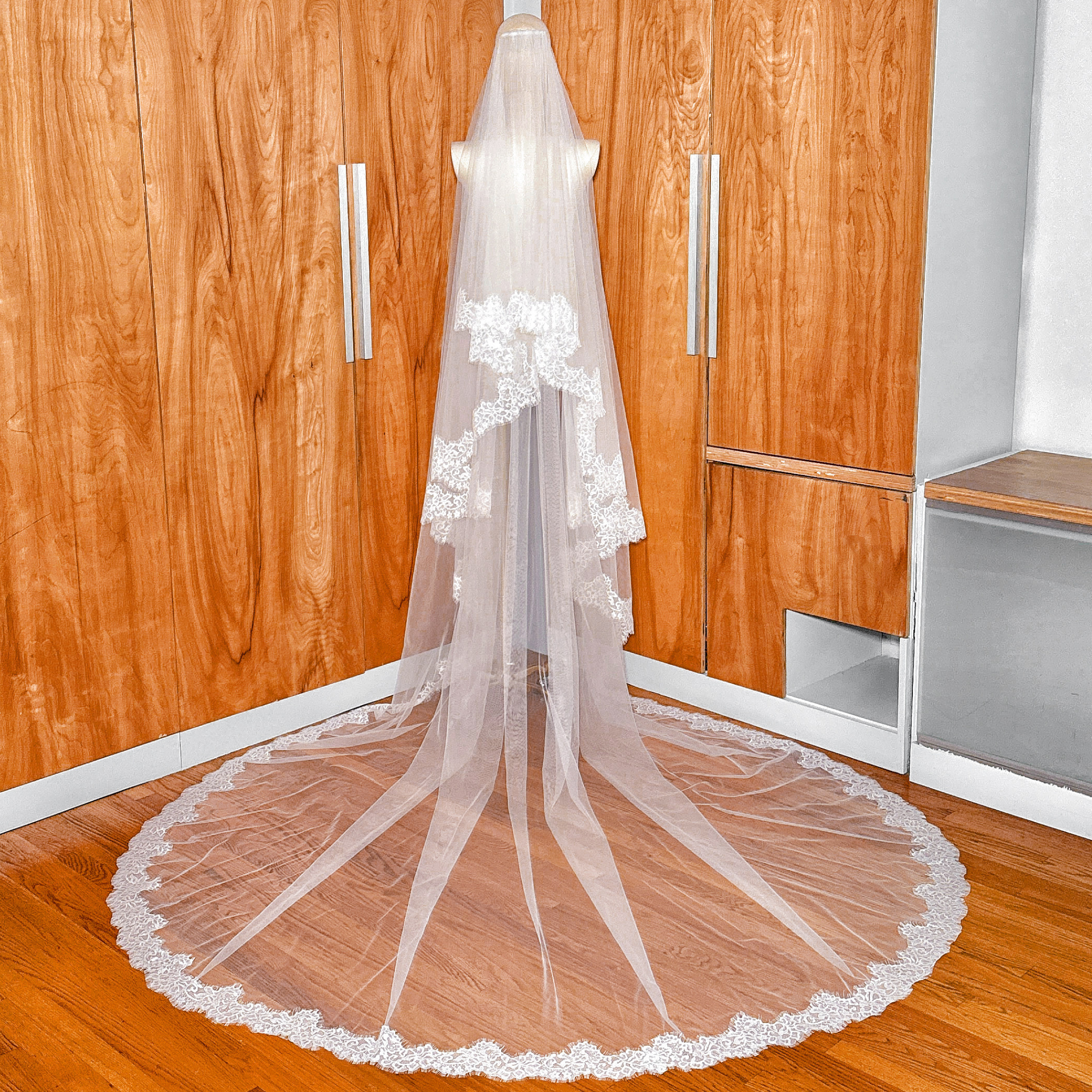 Back view of a cathedral length two tier Chantilly lace trim veil draped over a mannequin.