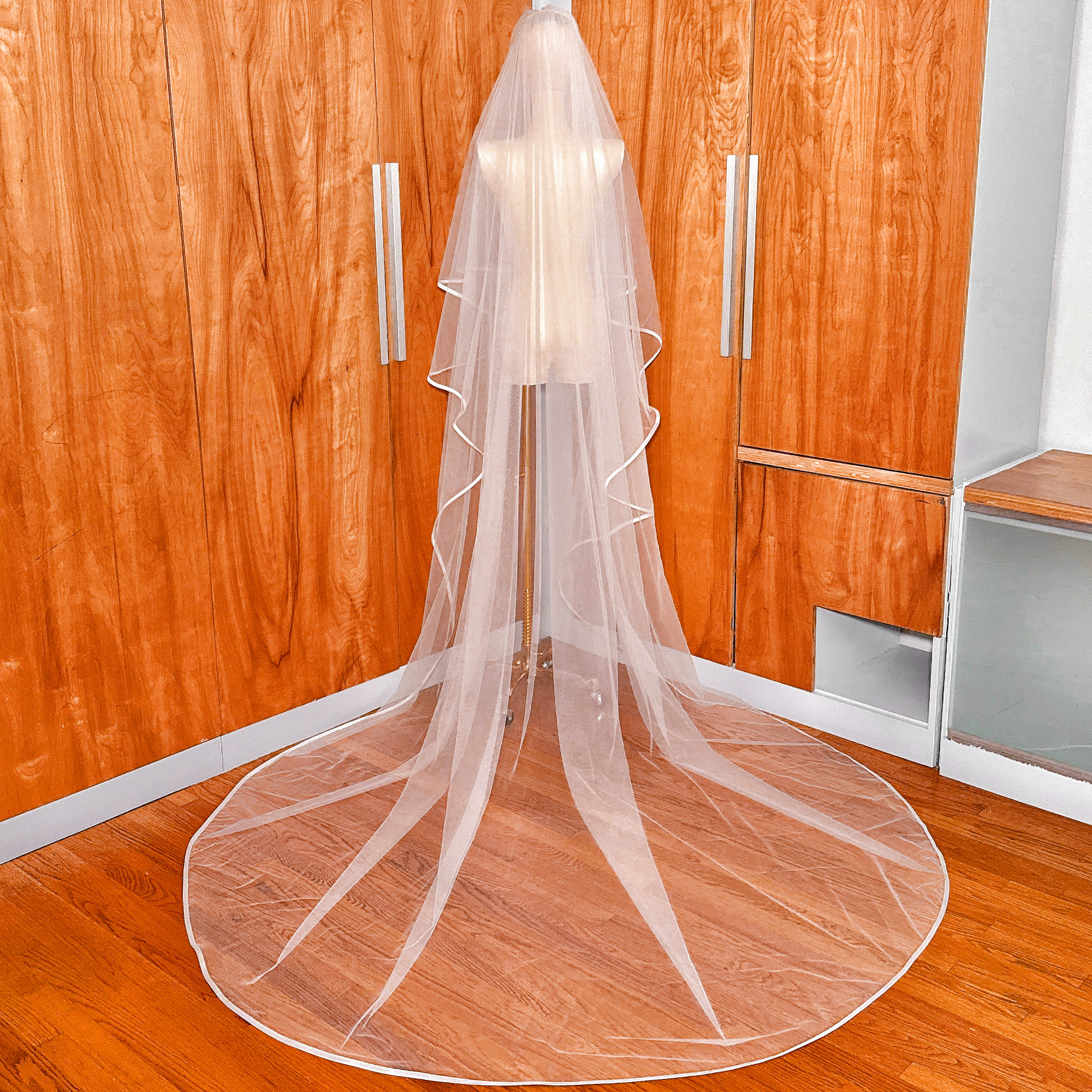 Back view of a two tier ribbon edge wedding veil with blusher flowing down in cathedral length on a mannequin.
