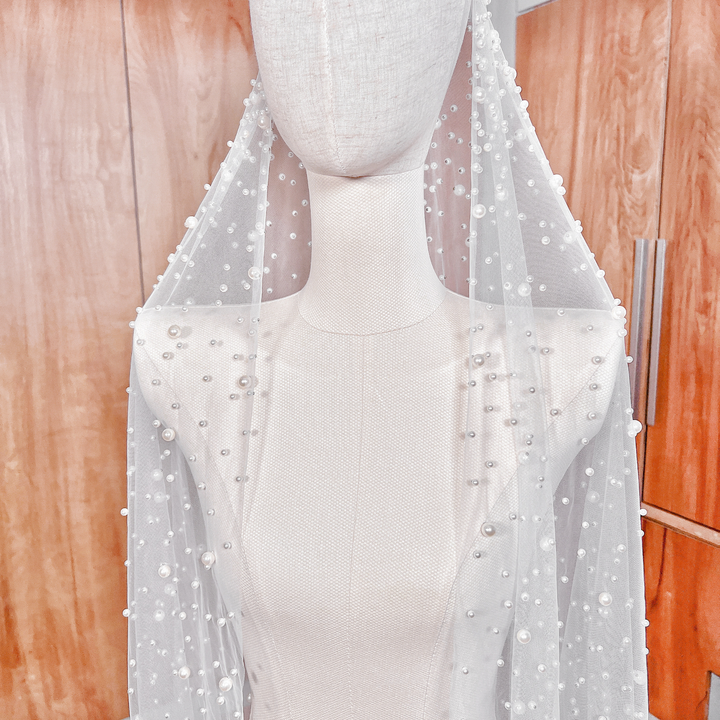 Side profile of a long cathedral wedding veil with pearl studs and a traditional mantilla edge.