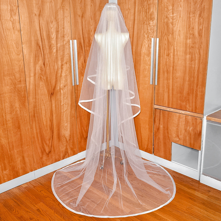 Back view of a cathedral length veil with 1 inch ribbon trim and blusher on a bridal mannequin.