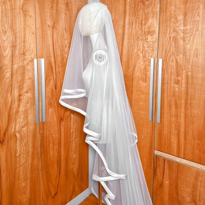 Elegant cathedral length bridal veil with 1 inch ribbon trim and blusher shown on a mannequin.