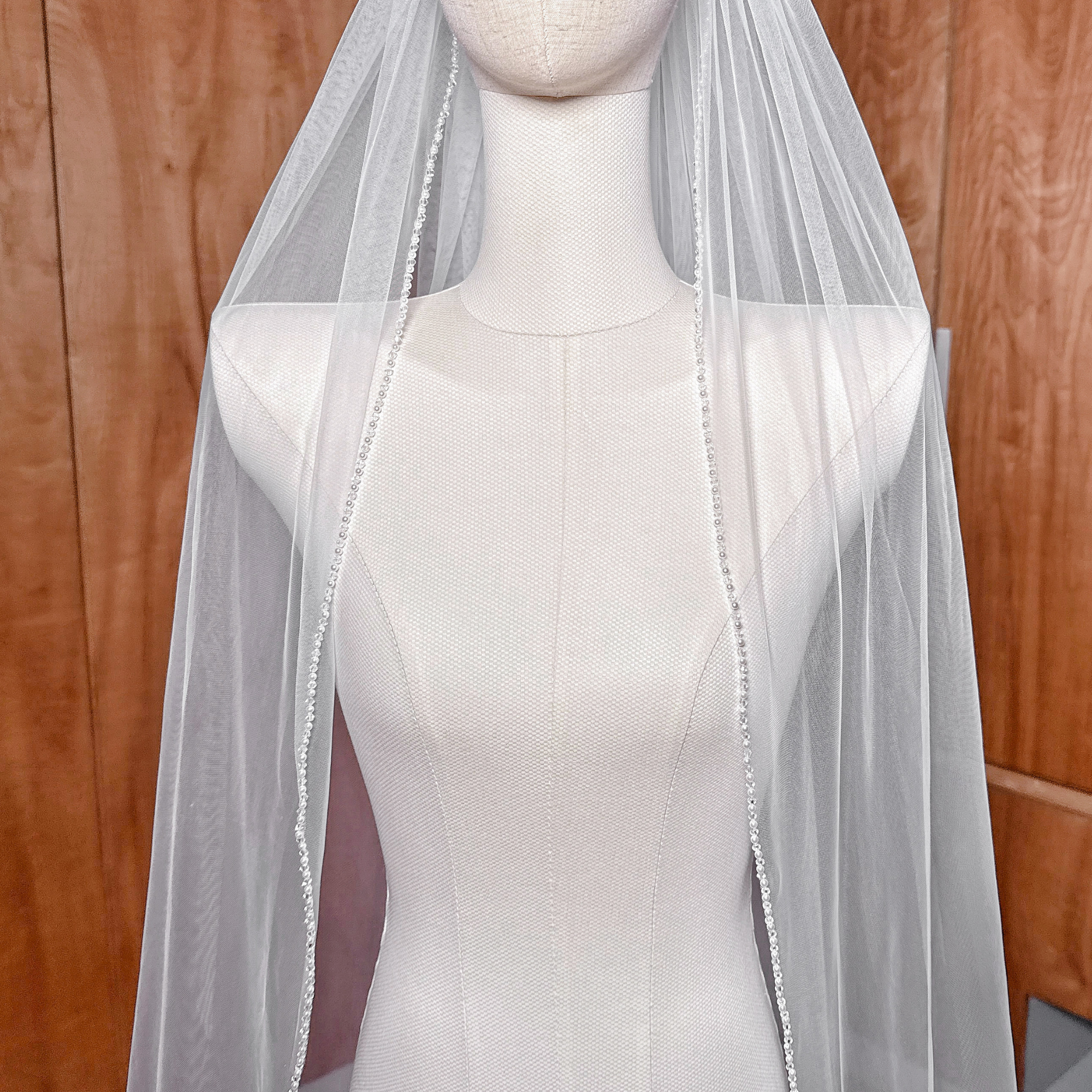 Close-up detail of the intricate pearl and crystal beading along the edge of a soft white cathedral bridal veil.
