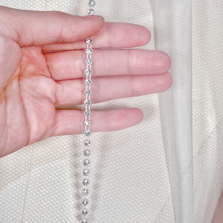 Close-up view of the sparkling crystal trim on a cathedral length rhinestone edge wedding veil.