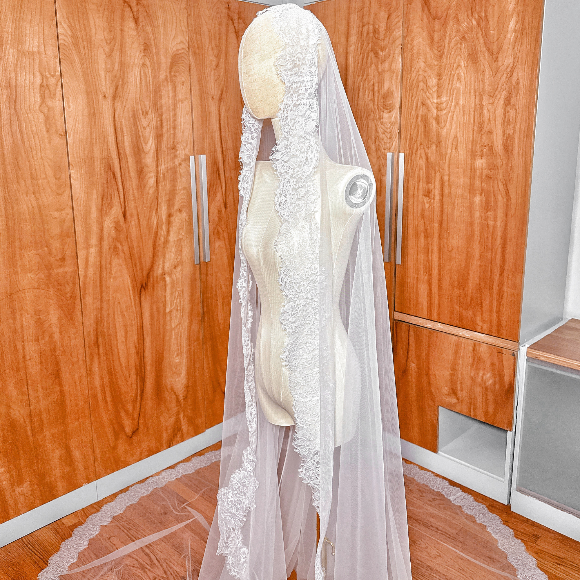 Full-length view of a Chantilly lace mantilla veil draped over a mannequin to show the cathedral length flow.
