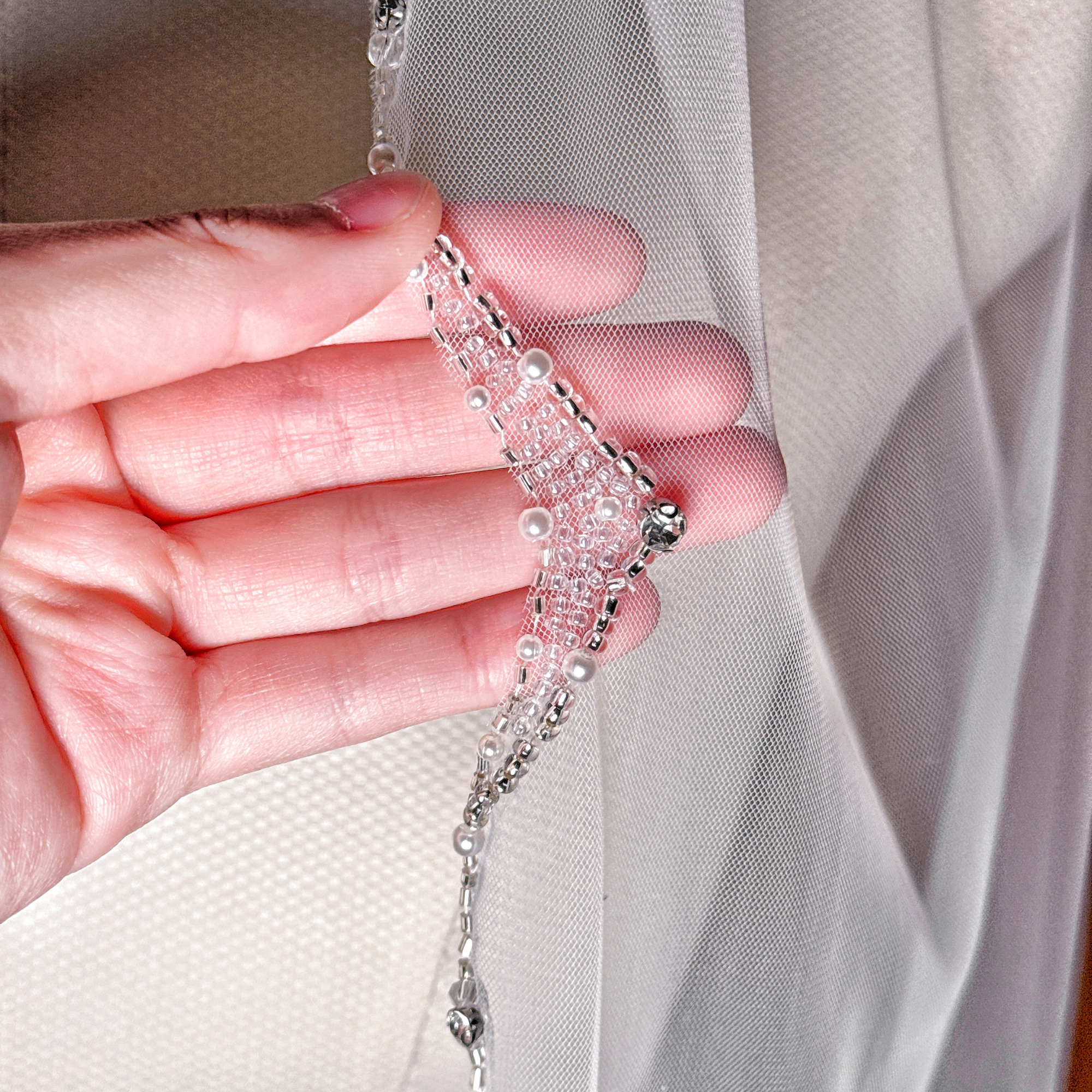Detailed close-up of the hand-stitched baby pearls and silver beads on the edge of a bridal fingertip veil.