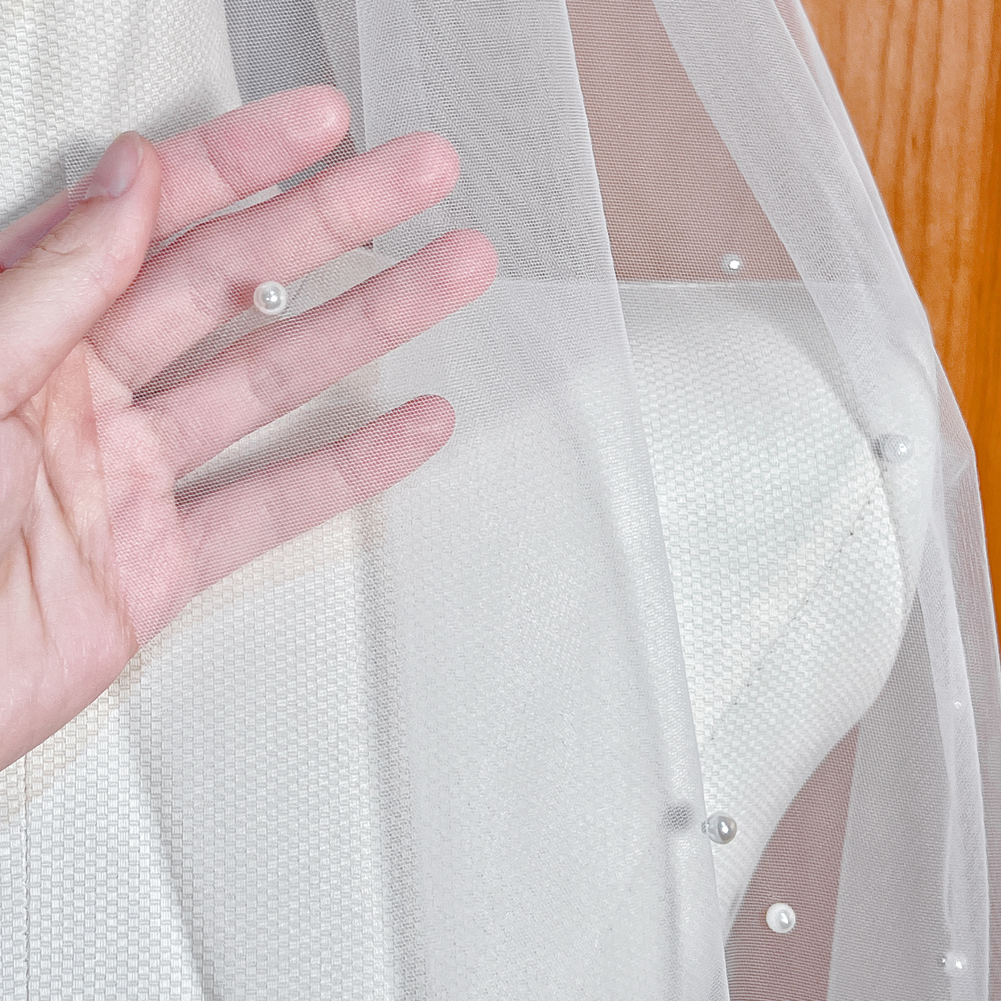 Detailed close-up of individual scattered pearls hand-applied to a fine ivory tulle wedding veil.