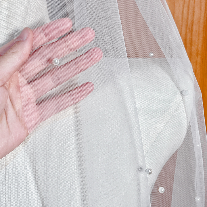 Detailed close-up of individual scattered pearls hand-applied to a fine ivory tulle wedding veil.