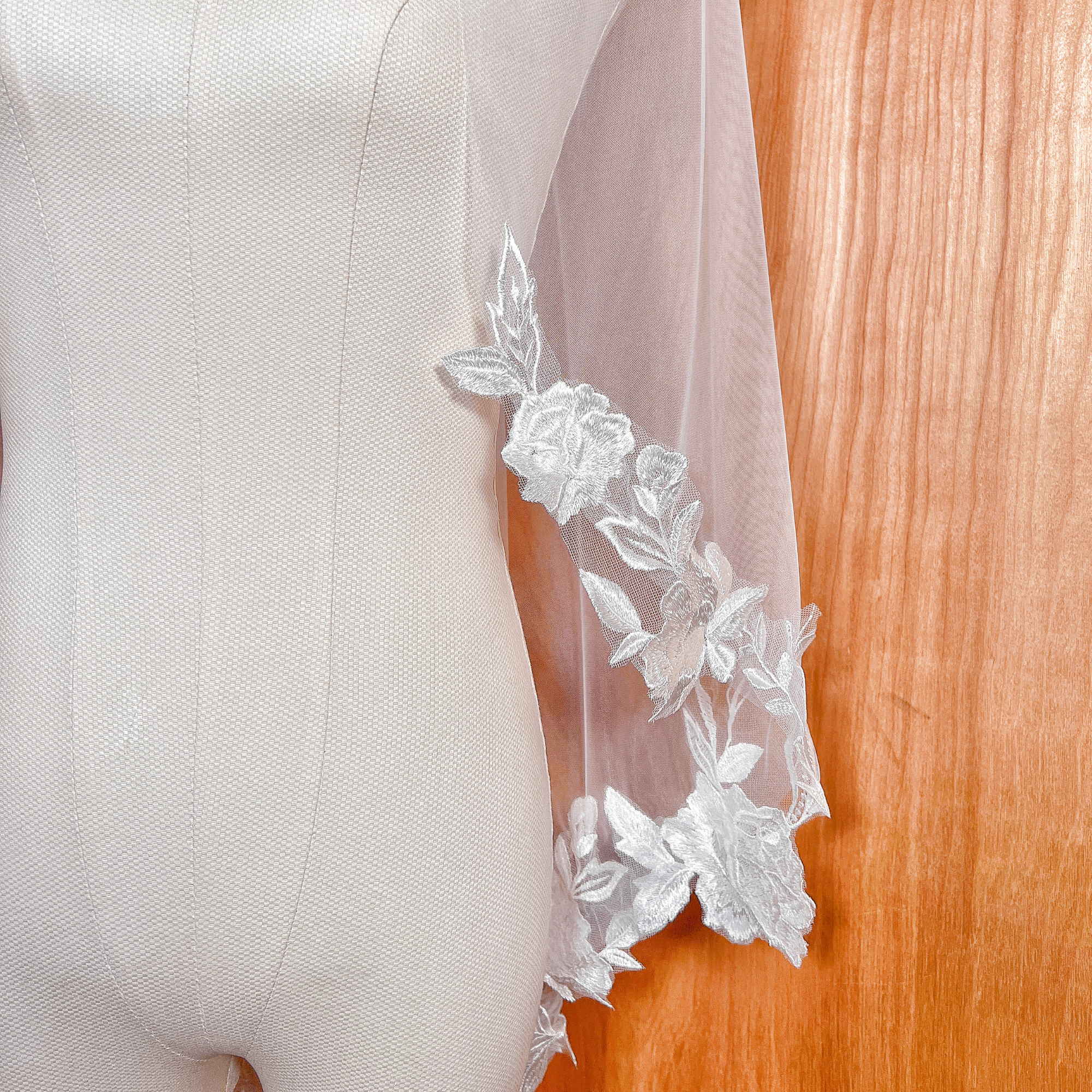 Close-up of 3D floral appliqués on a fingertip-length wedding veil, showing high-quality embroidery and petal textures on an ivory mannequin.