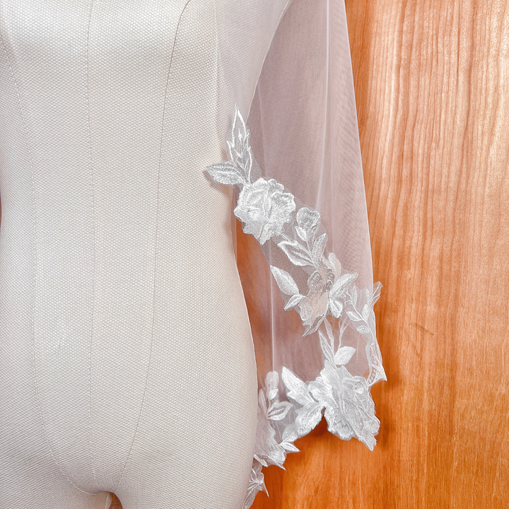 Close-up of 3D floral appliqués on a fingertip-length wedding veil, showing high-quality embroidery and petal textures on an ivory mannequin.