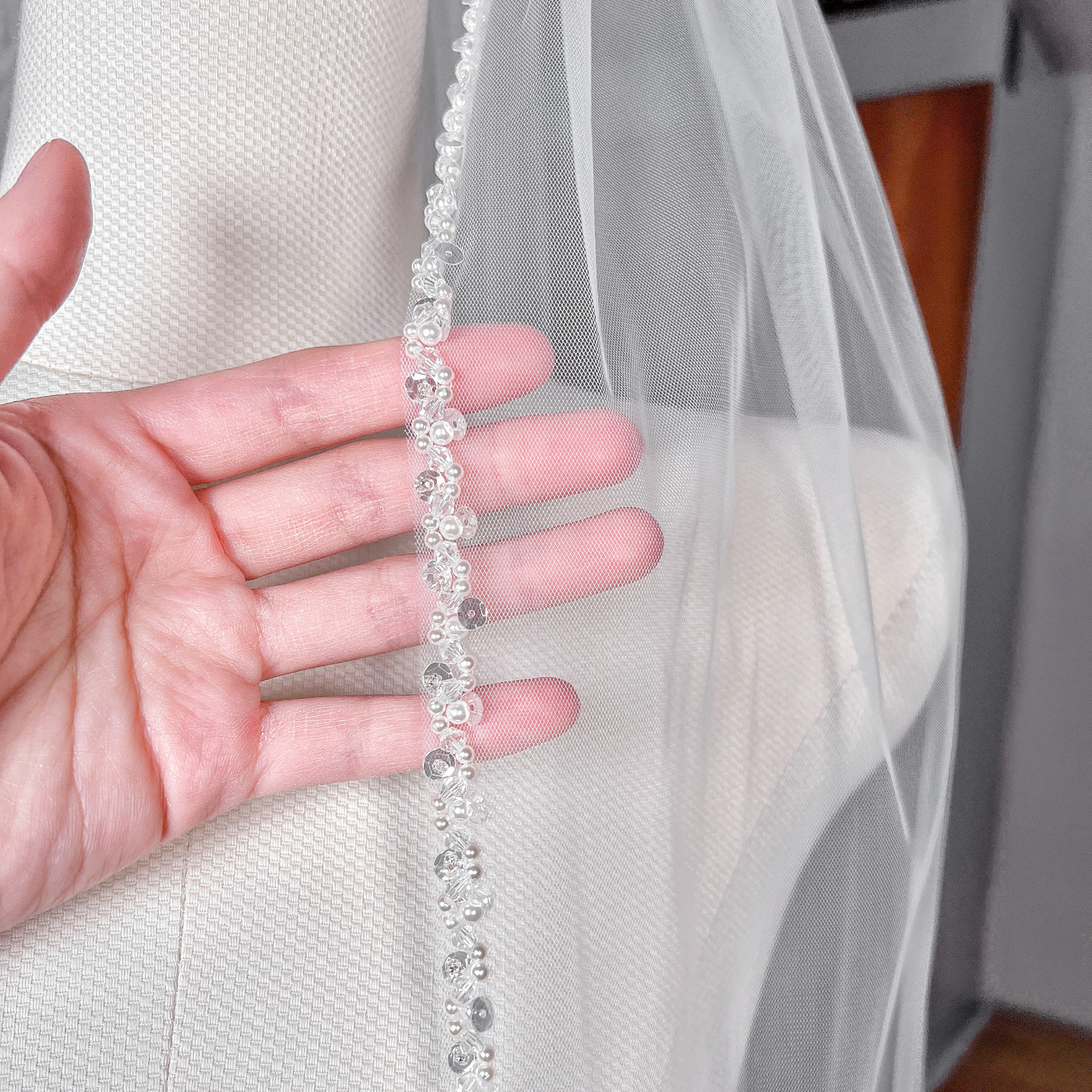Detailed close-up of the hand-stitched pearl trim along the border of a sheer cathedral wedding veil.