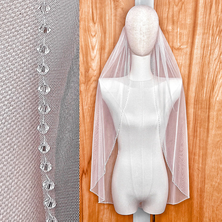Front view of a fingertip length crystal beaded edge wedding veil on a mannequin.