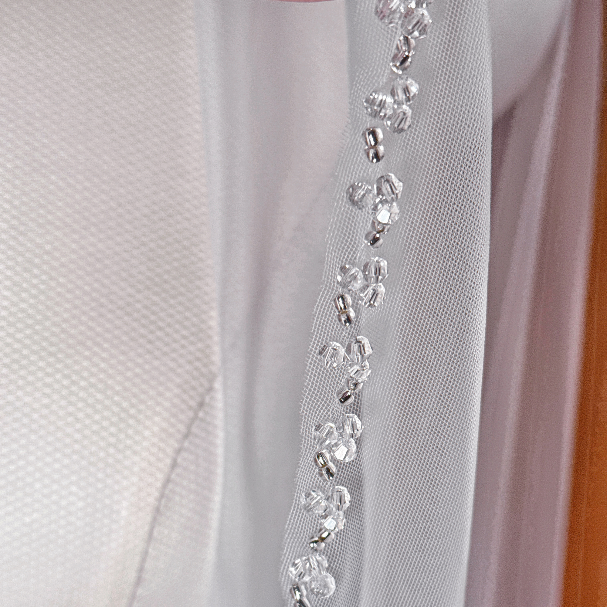 Sharp focus on the glittering trim of a waltz length crystal beaded edge wedding veil.