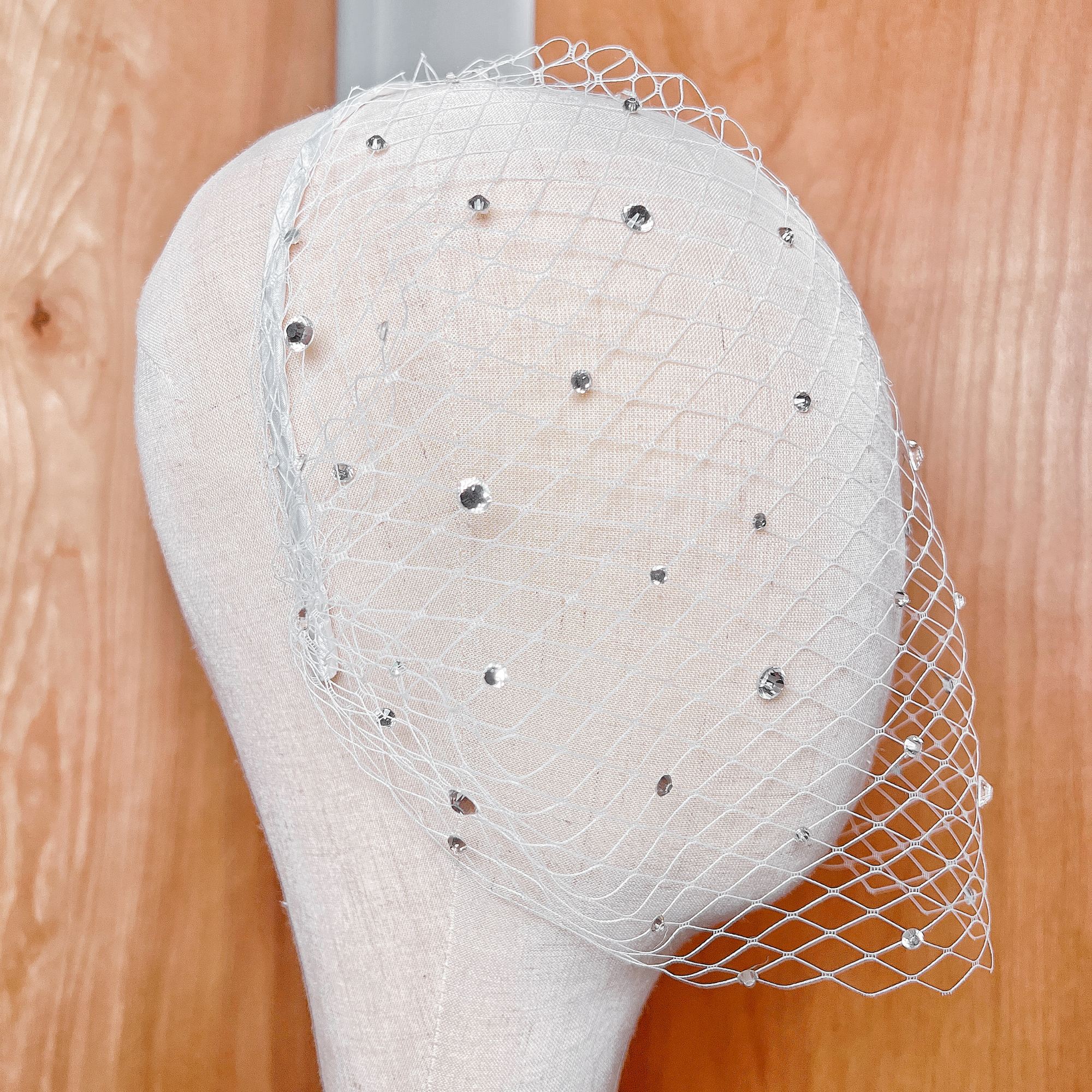 Close-up of a crystal birdcage wedding veil with rhinestone accents displayed on a mannequin head.