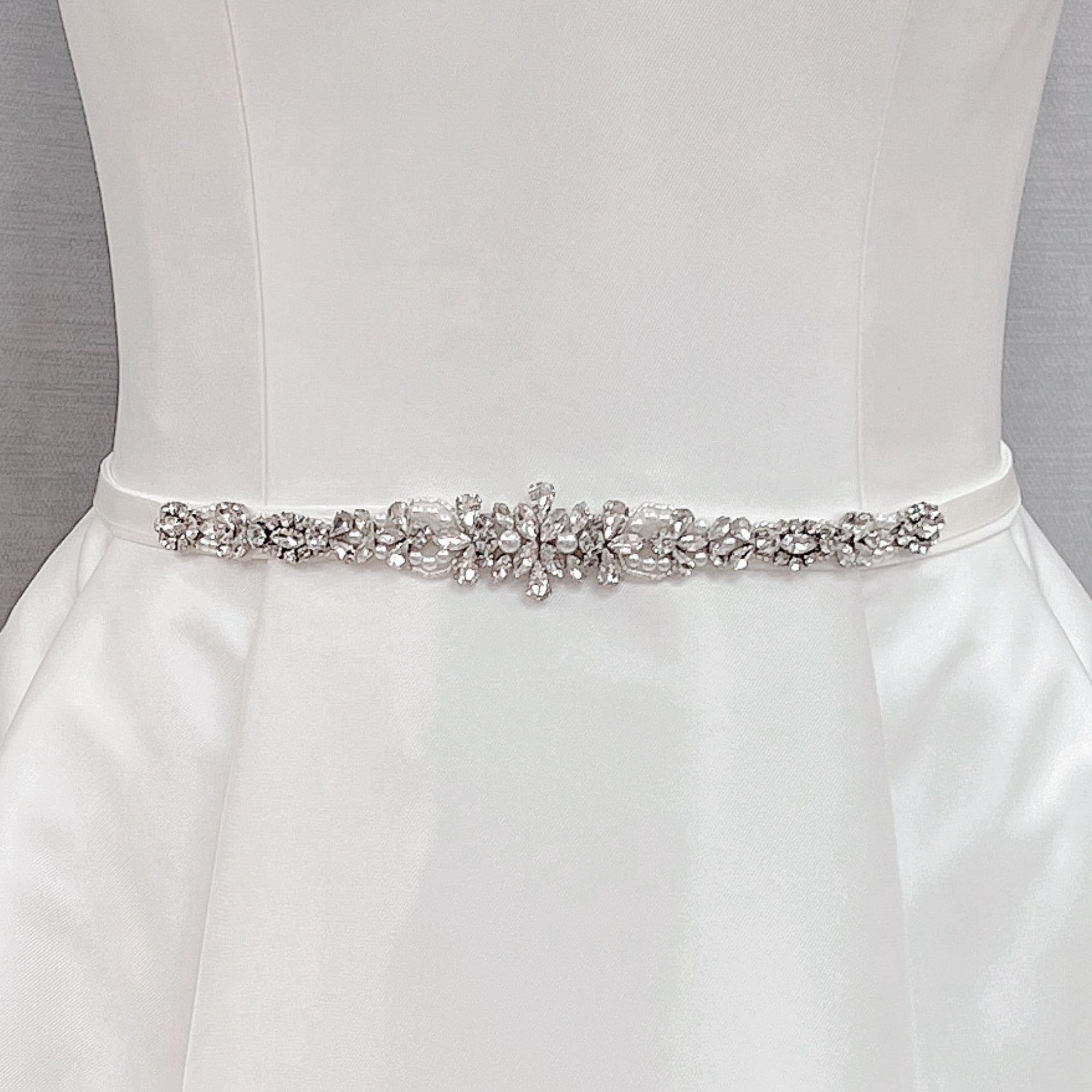 Crystal rhinestone and pearl bridal belt displayed on a dress mannequin.
