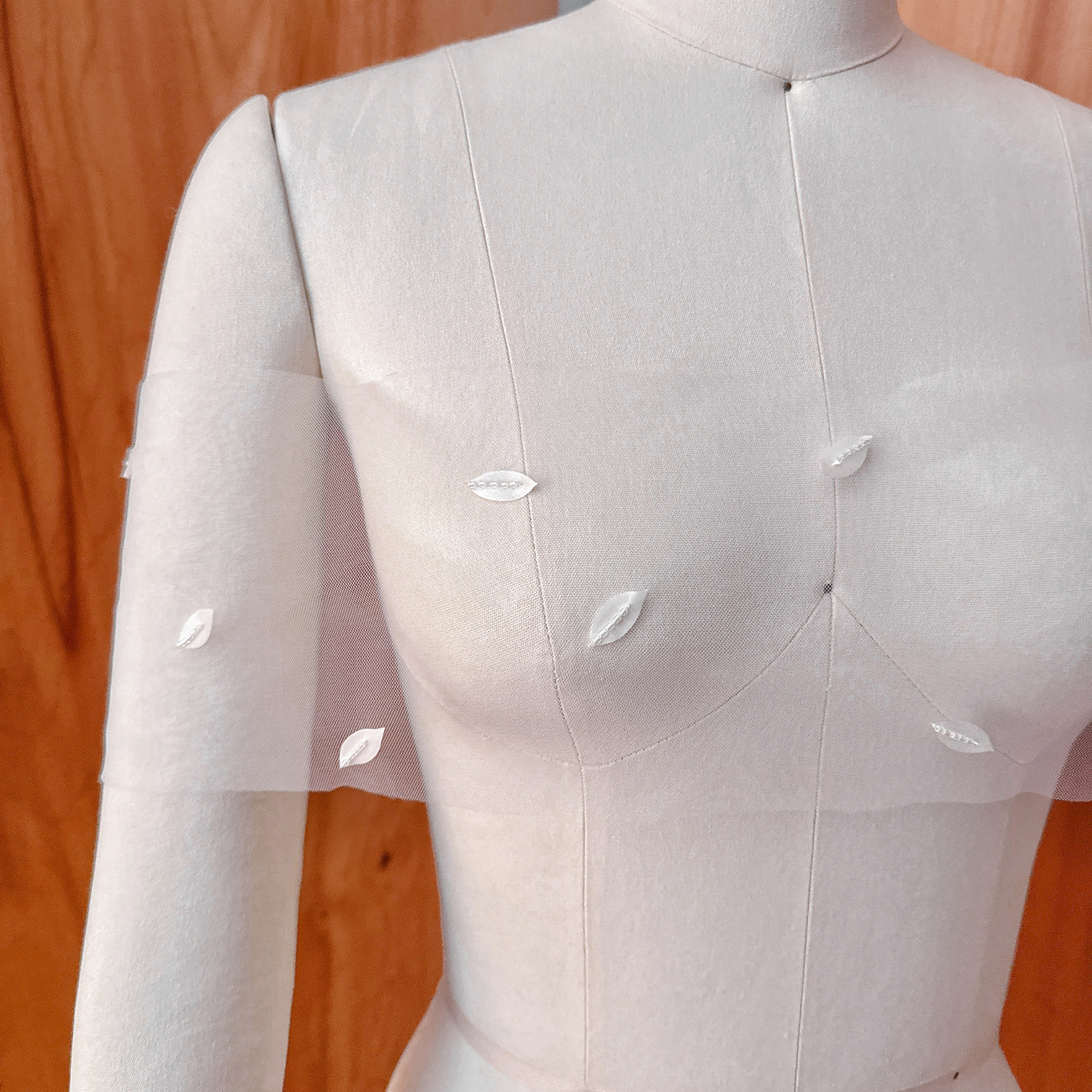 A front close-up view of a sheer white illusion bridal wrap featuring handcrafted 3D silk petals and hand-beaded seed beads, displayed on a classic fabric dressmaker mannequin.