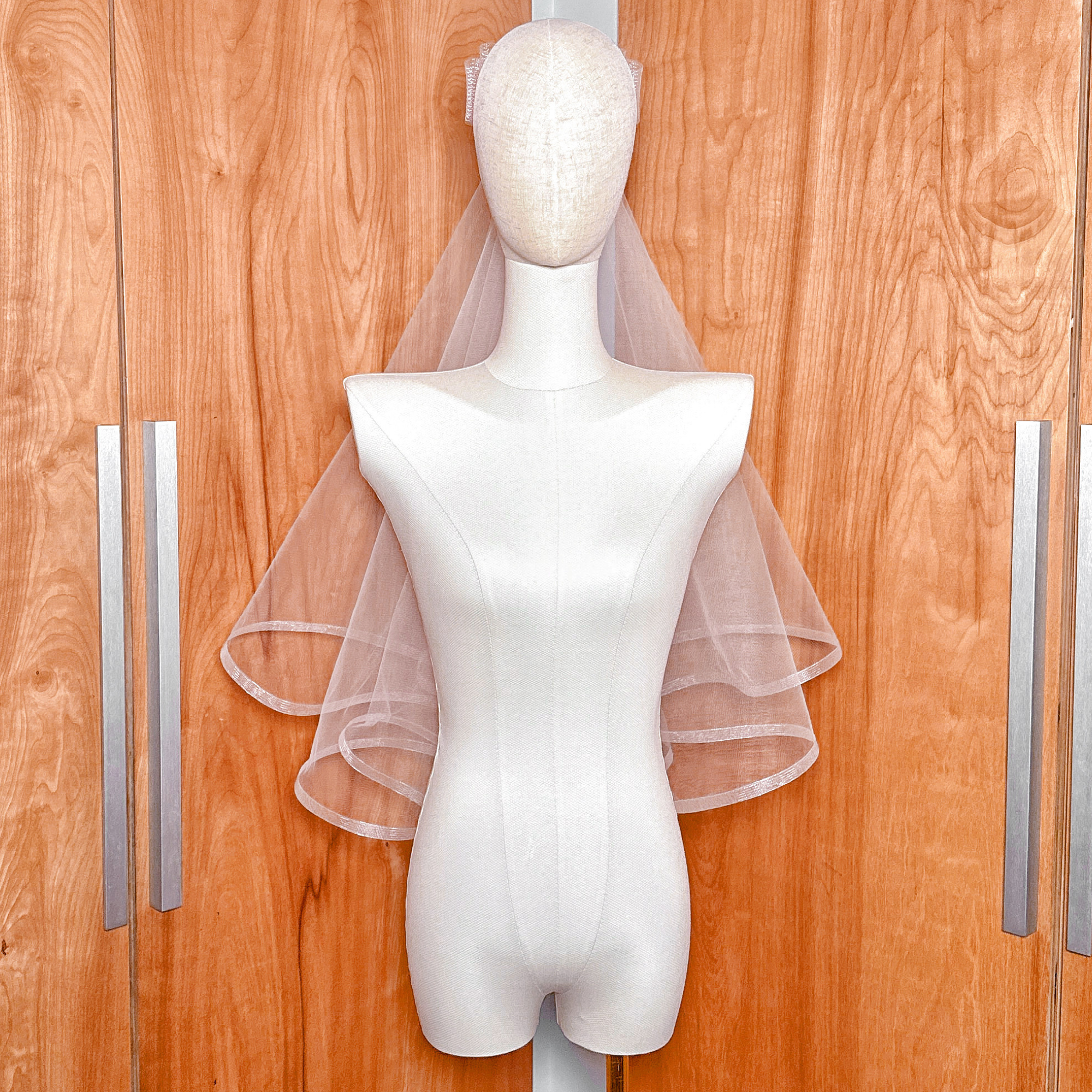 Front view of a two tier elbow length wedding veil with horsehair trim and bow detail on a mannequin.
