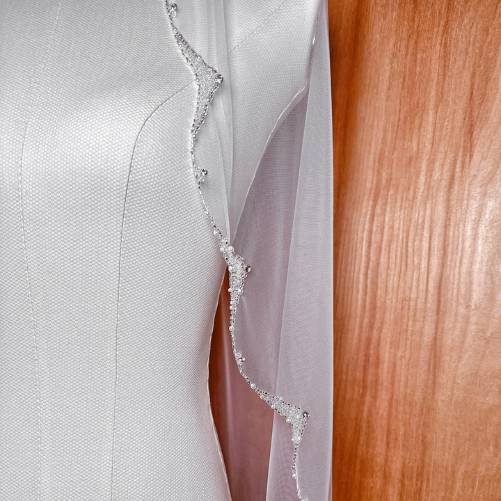 High-resolution shot showcasing the texture of bridal illusion tulle and lustrous pearl trim on a fingertip veil.
