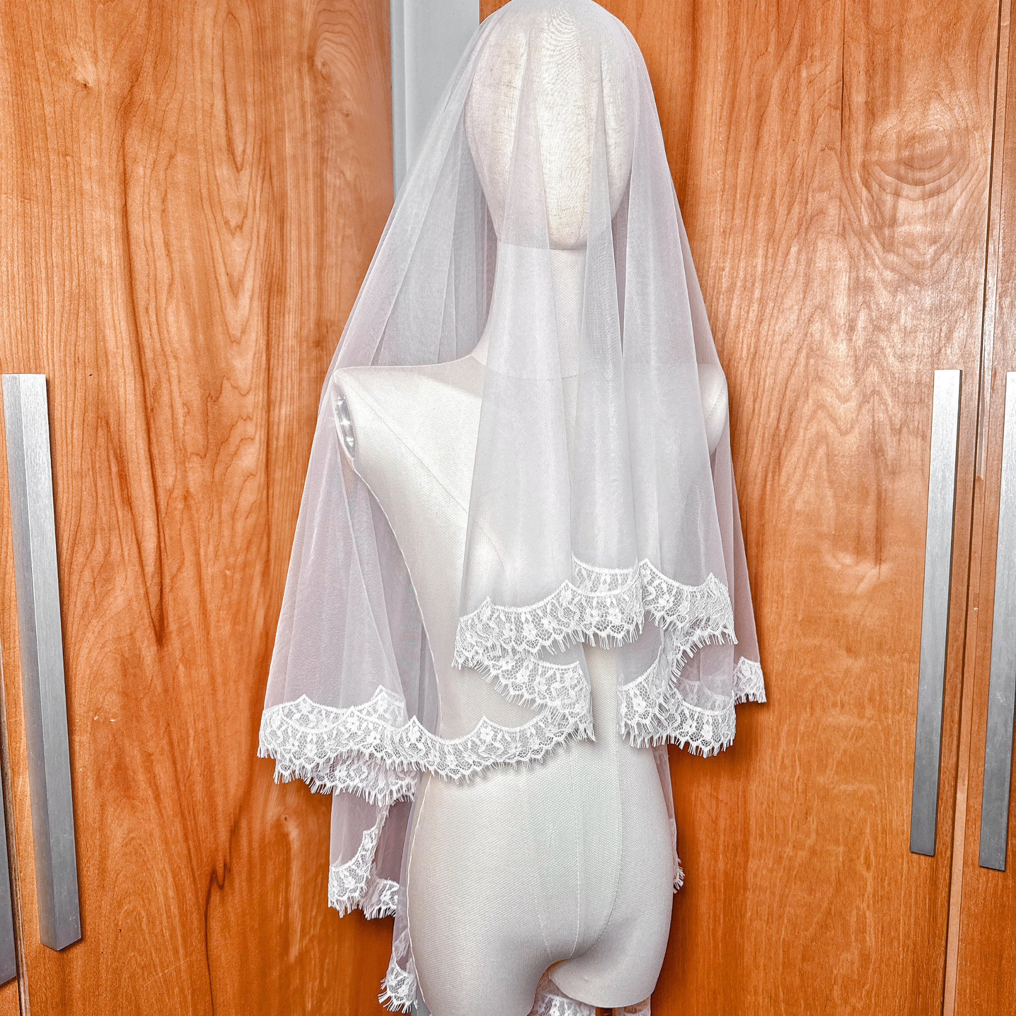 Elegant hip-length bridal drop veil with a delicate lace border, styled on a mannequin in a studio setting.