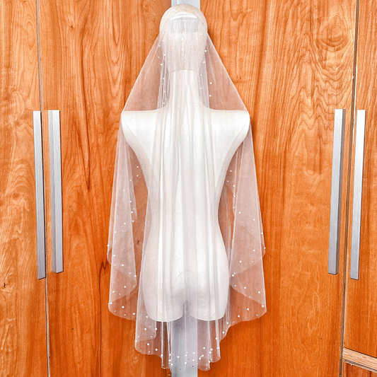 Elegant fingertip length wedding veil featuring a scattered pattern of pearls and rhinestones for a classic bridal look.