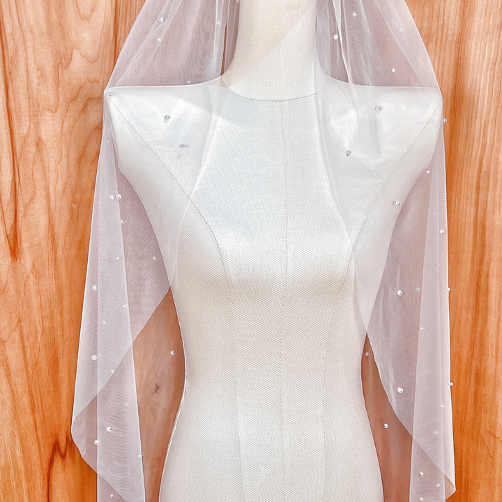 Full-length display of a scattered pearl bridal veil, showing how the fingertip length falls gracefully to create a romantic and modern bridal silhouette.