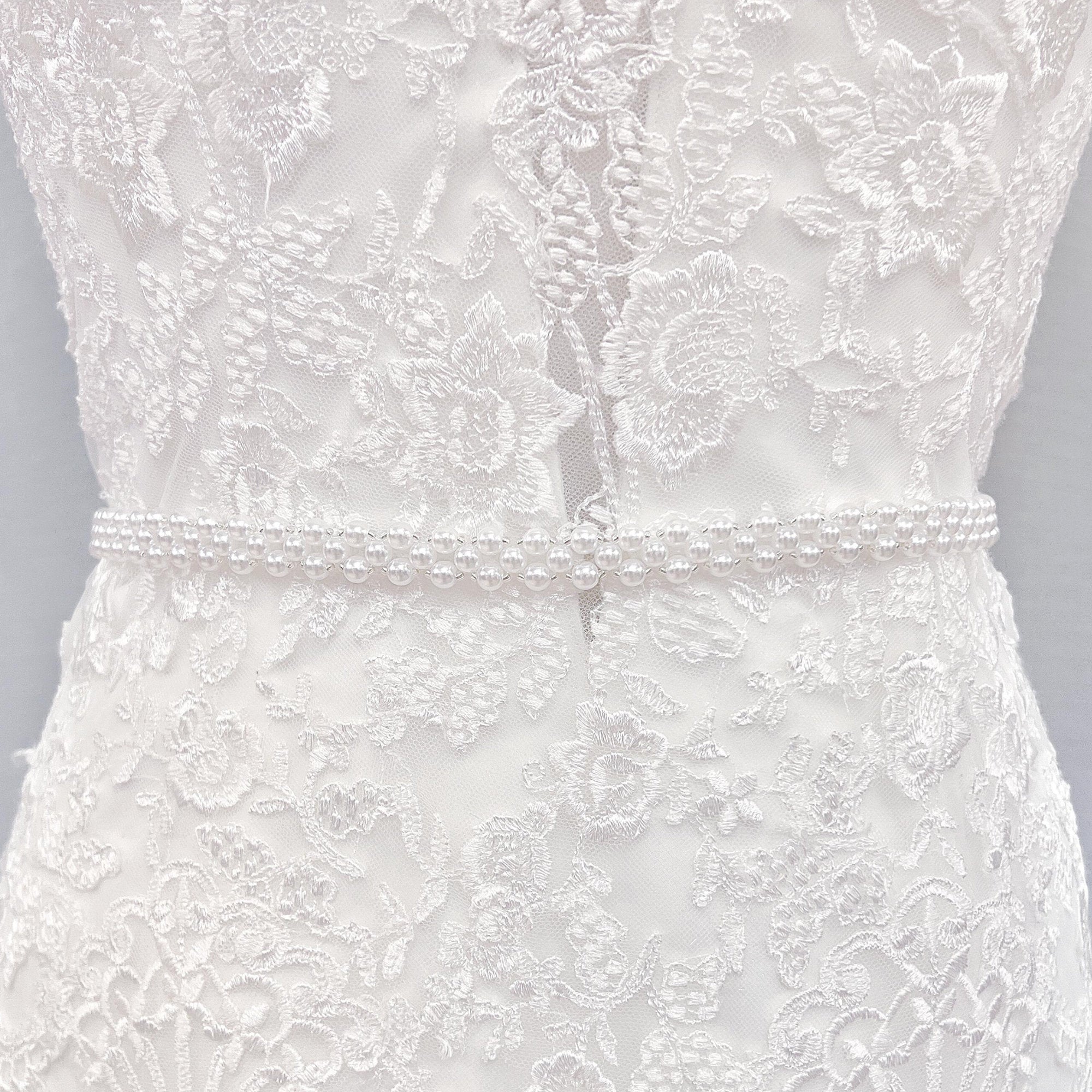 Elegant simple pearl bridal belt tied around the waist of an A-line wedding dress.