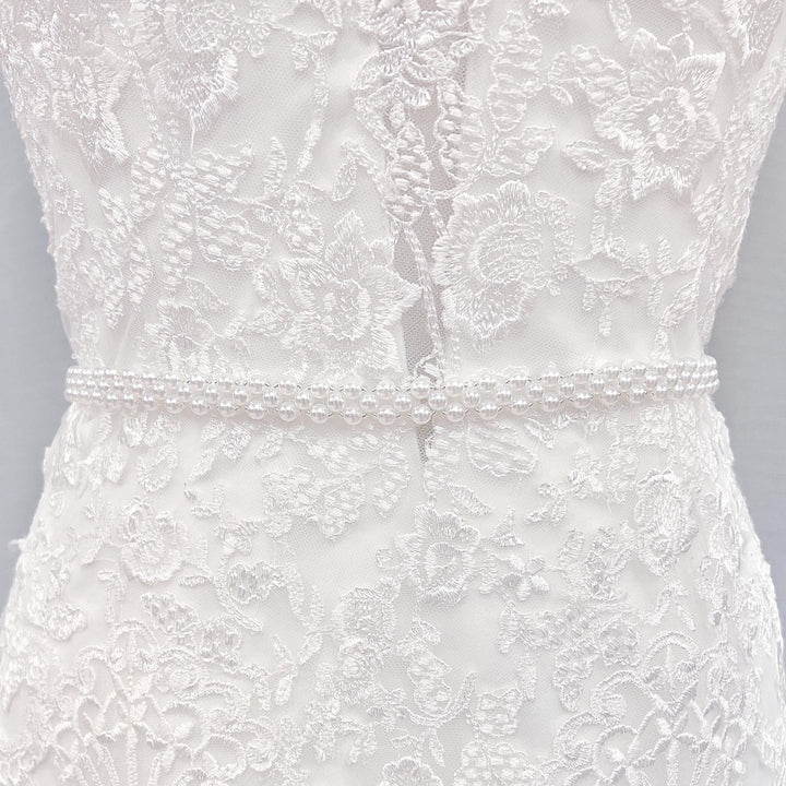 Elegant simple pearl bridal belt tied around the waist of an A-line wedding dress.