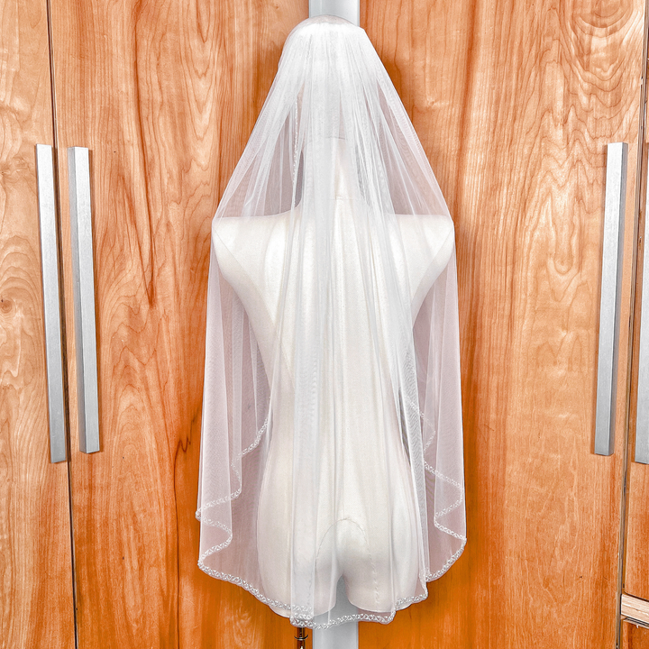 A luxurious soft tulle wedding veil with a pearl beaded edge displayed in a fingertip length style.