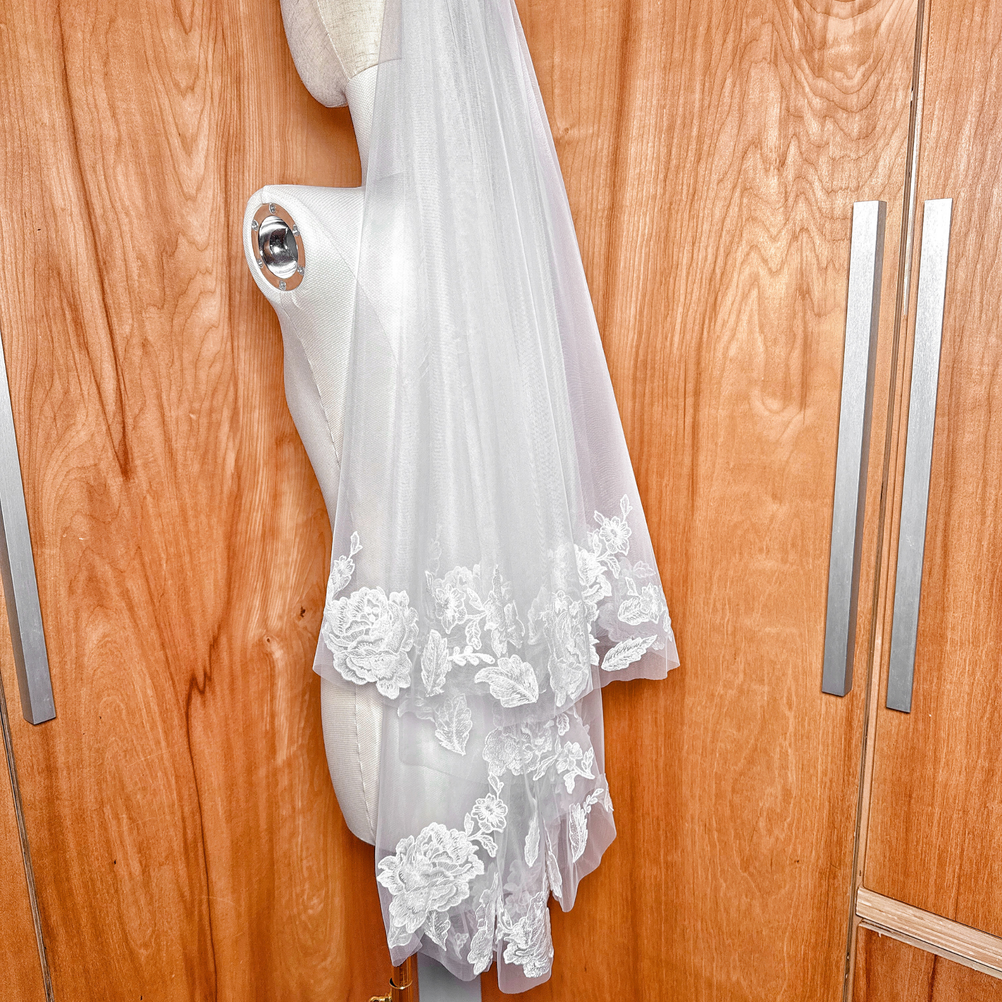 Elegant two tier floral lace wedding veil draped over a mannequin, showing fingertip length layers.