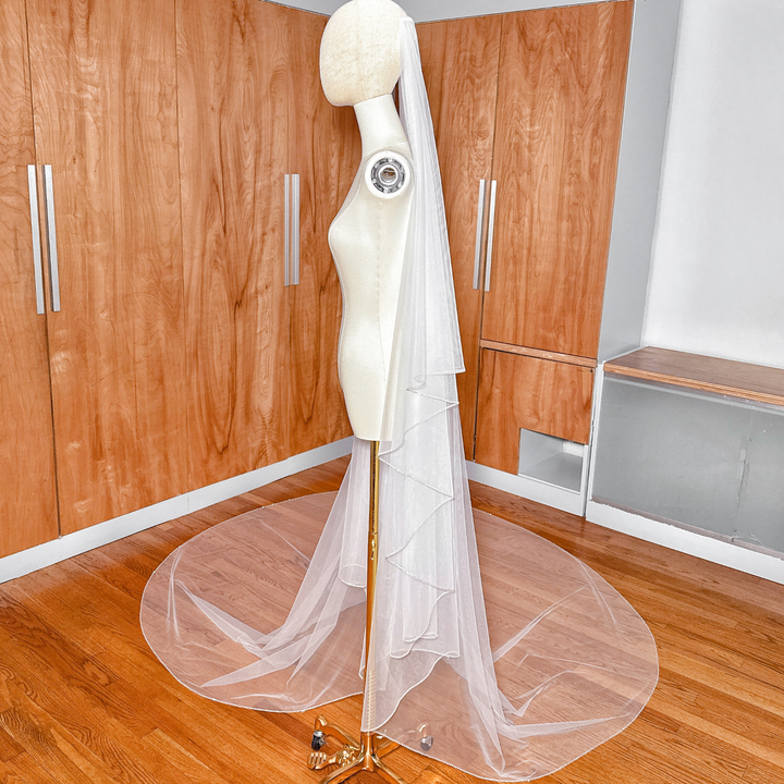 Angled display of an elegant two-tier wedding veil with a rhinestone edge flowing down in cathedral length.