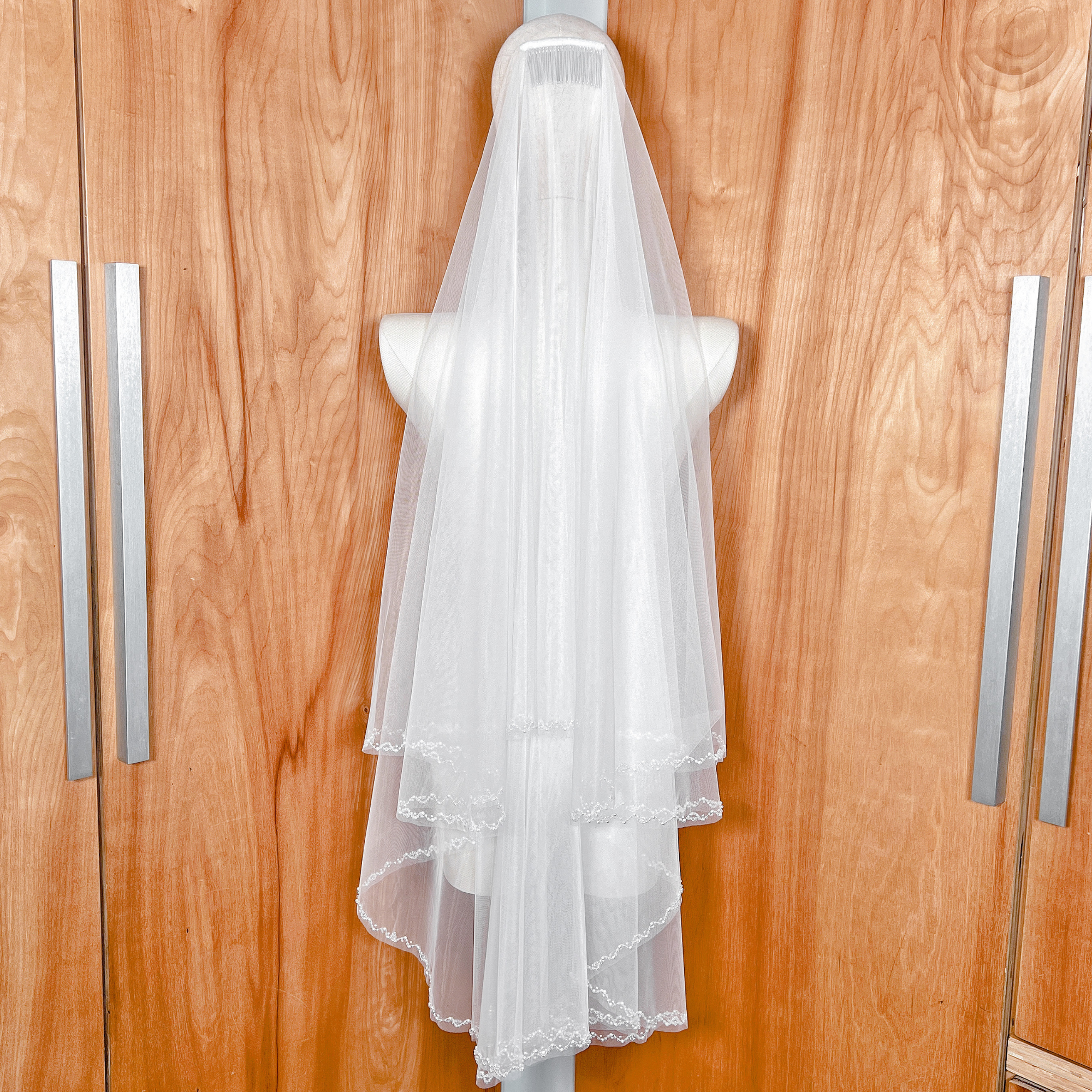 Back view of an elegant two-tier wedding veil with beaded edges draped in fingertip length.