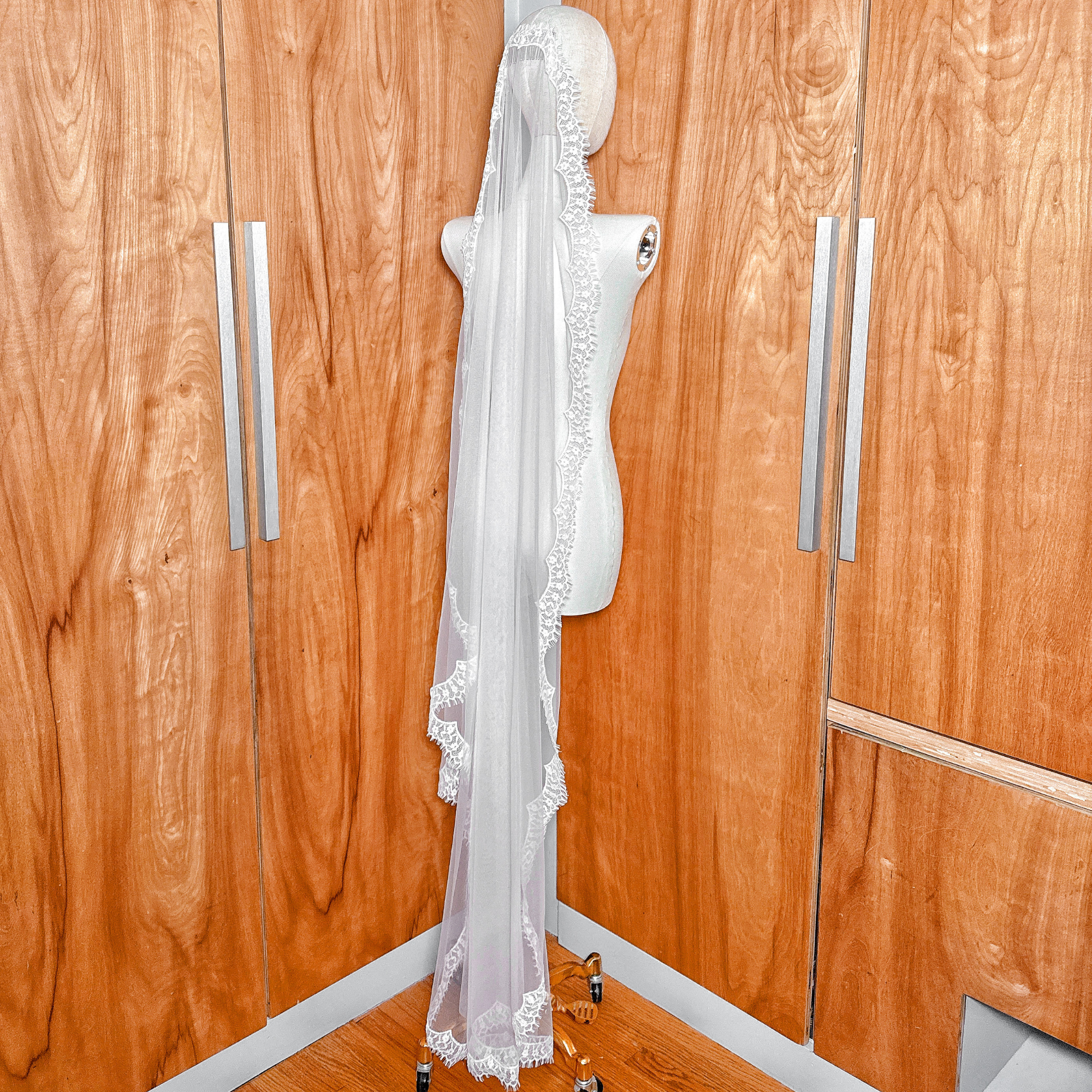 Rear view of a sheer waltz length eyelash lace mantilla veil draped over a mannequin's shoulders.