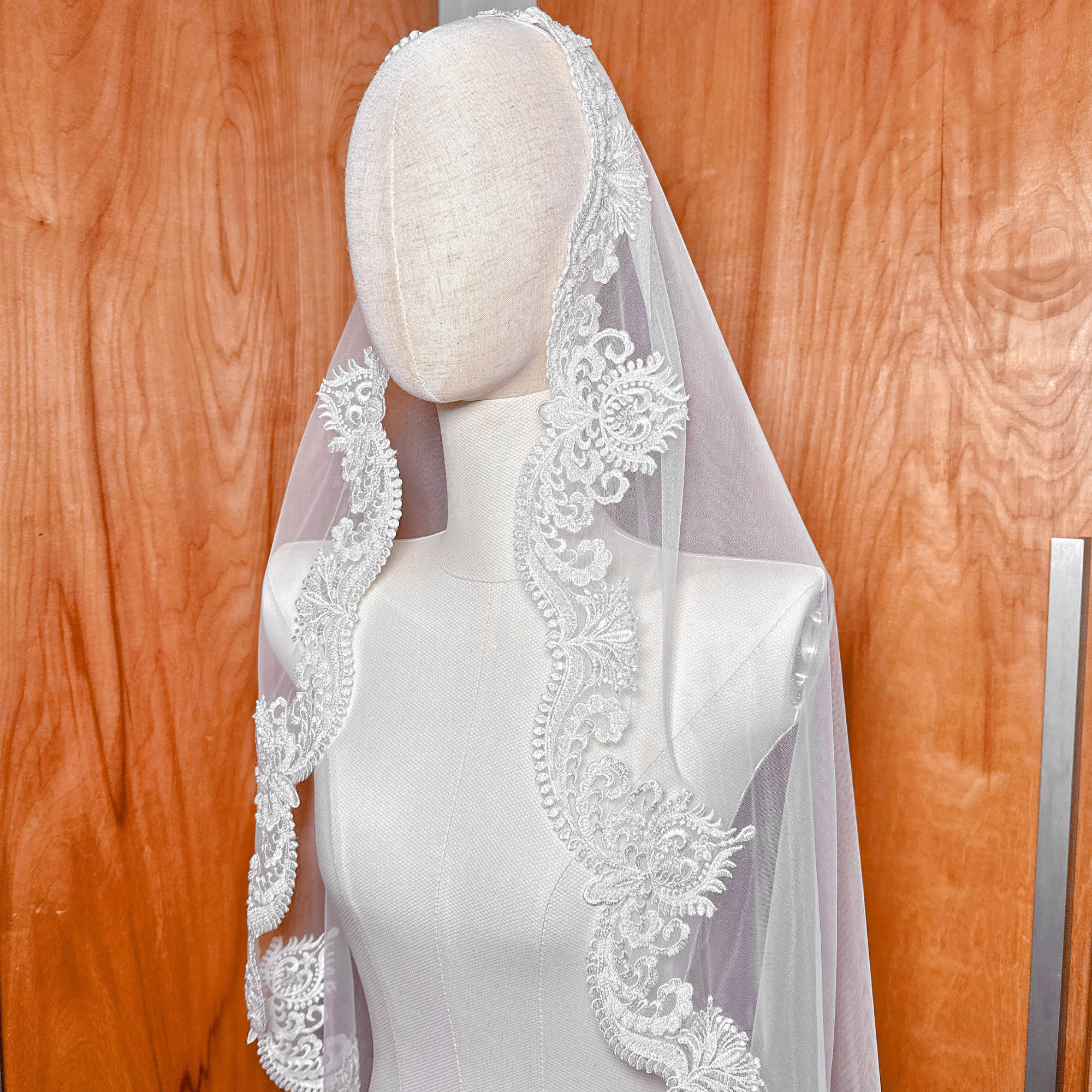 A fingertip length Beaded Scalloped Lace Mantilla Veil gracefully pinned to a mannequin, showcasing the scalloped floral lace trim.