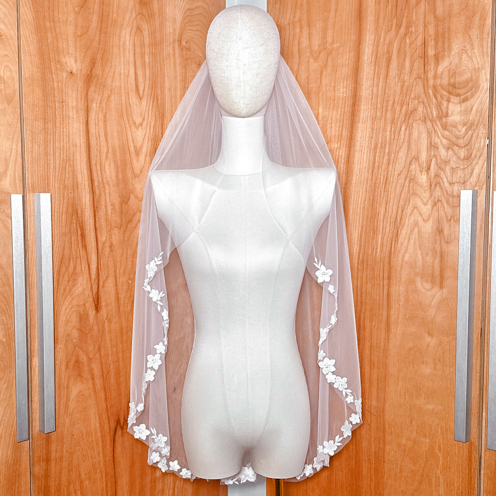 Front view of a fingertip length bridal veil with cascading floral lace displayed on a mannequin.