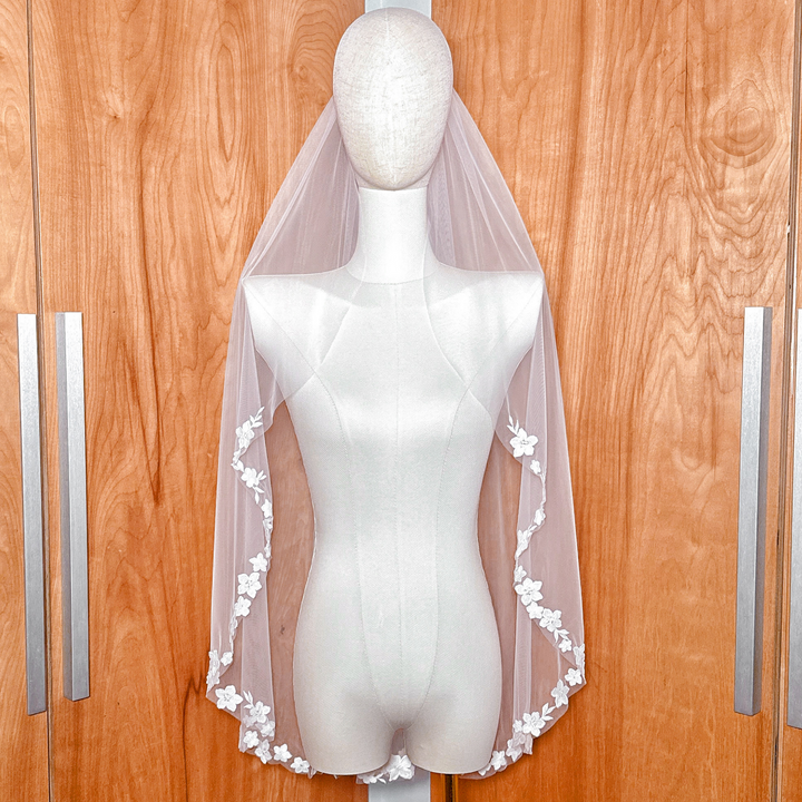 Front view of a fingertip length bridal veil with cascading floral lace displayed on a mannequin.