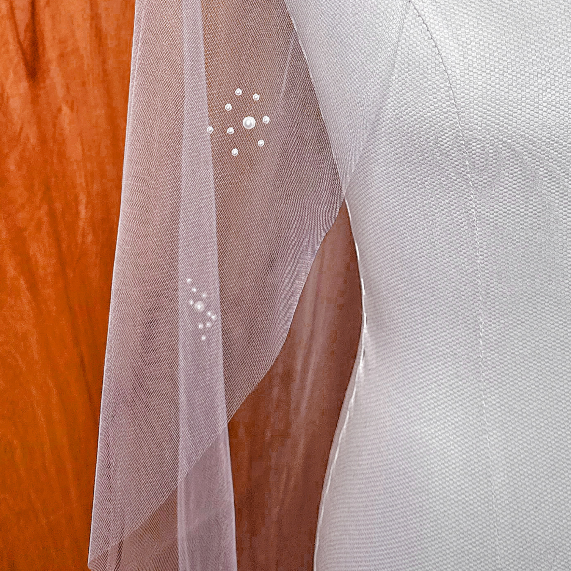 Close-up view of the intricate pearl cluster detailing on a fingertip-length wedding veil, showing the varied sizes of shimmering pearls.