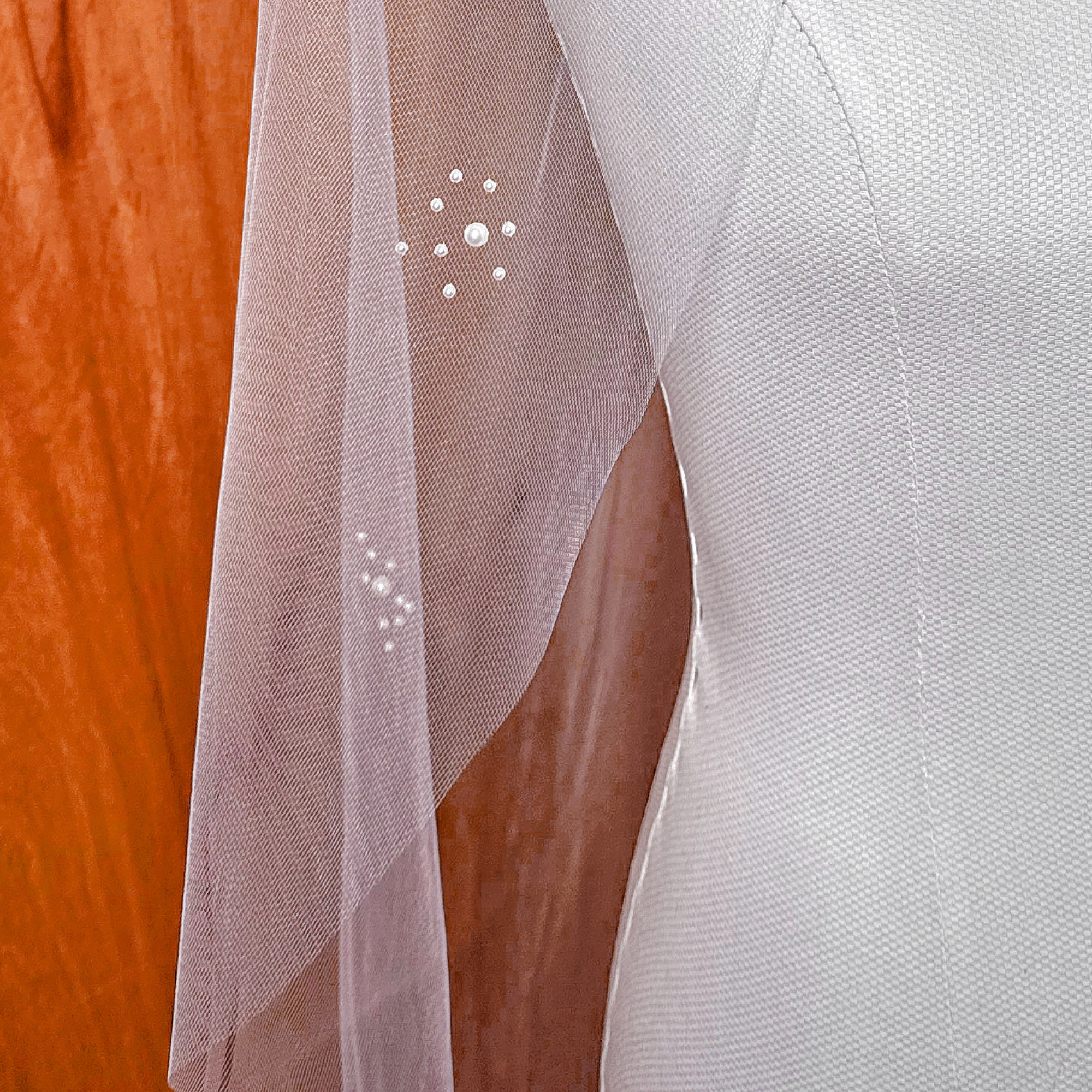 Close-up view of the intricate pearl cluster detailing on a fingertip-length wedding veil, showing the varied sizes of shimmering pearls.