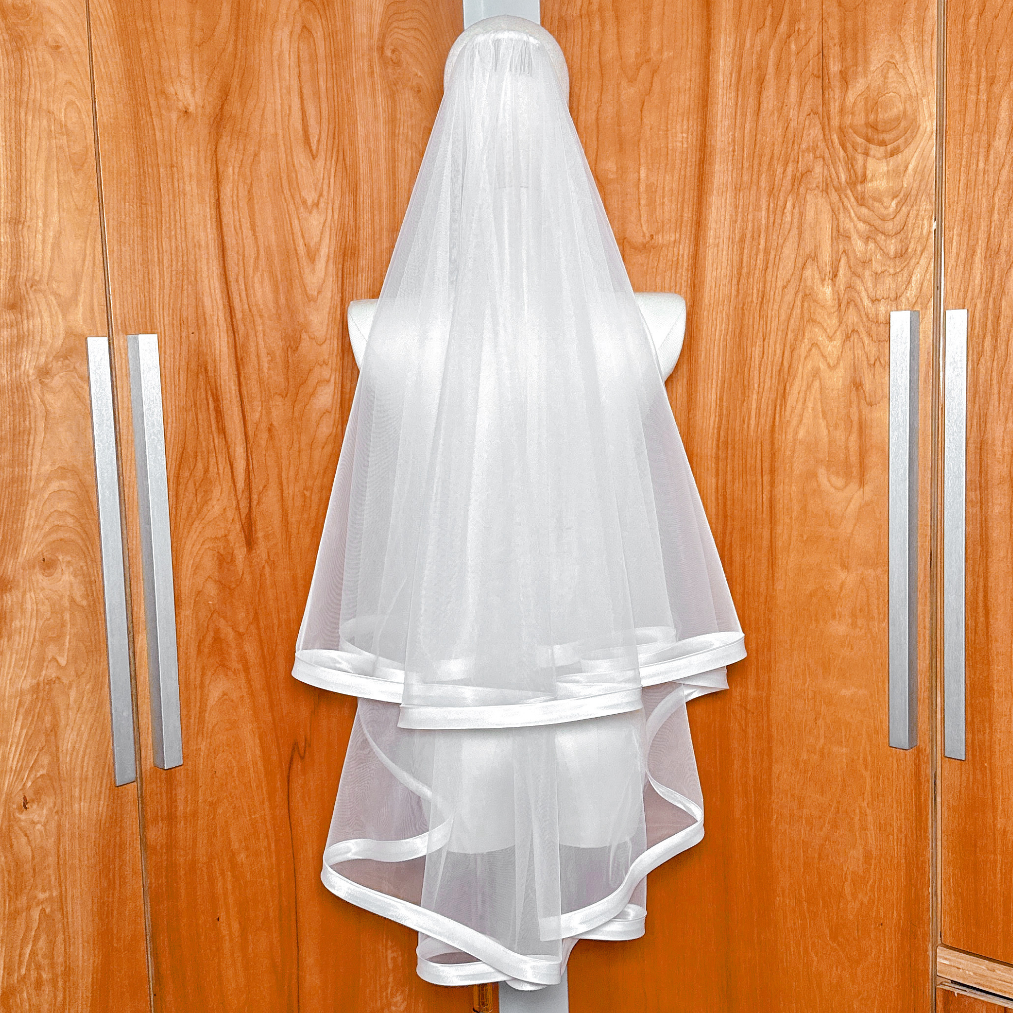 Sheer bridal tulle fingertip length veil with a structured 1-inch ribbon edge and blusher layer.