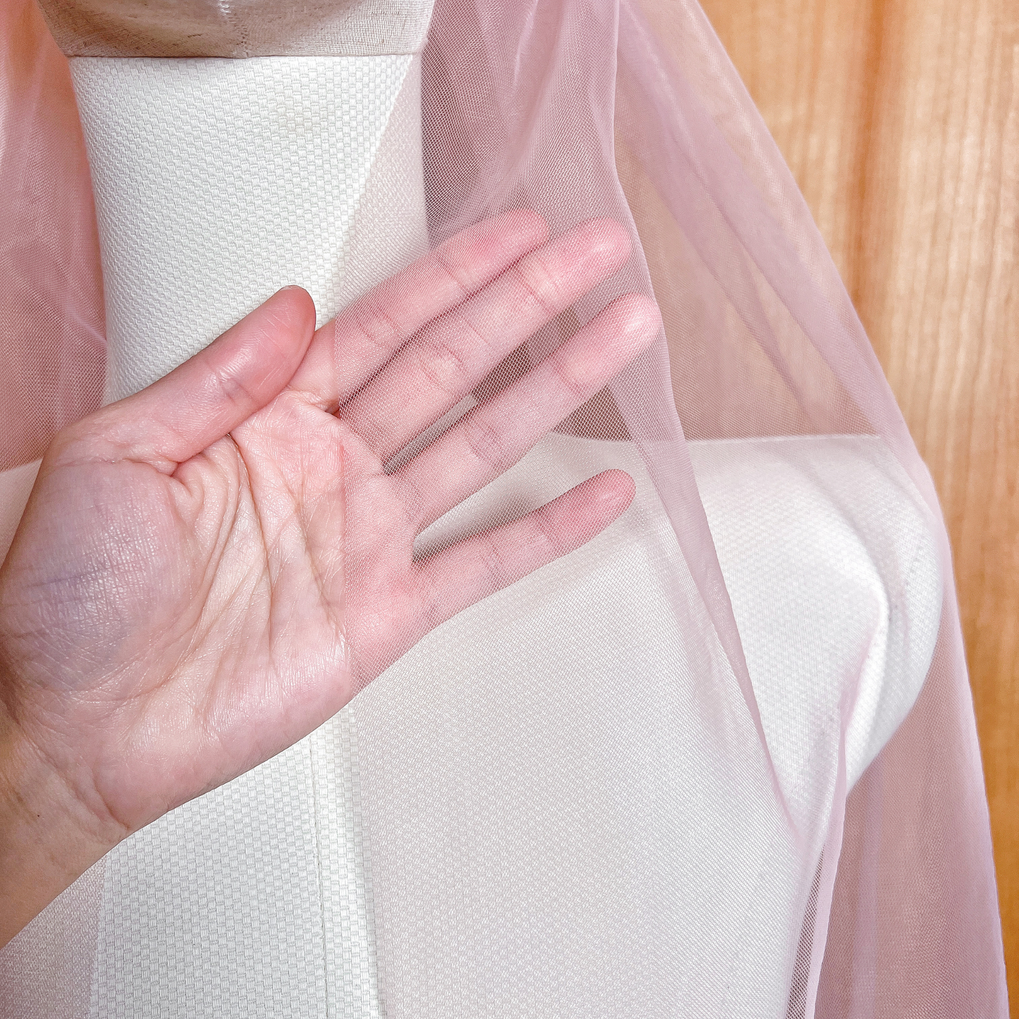 Close-up of the sheer blush pink tulle on a fingertip length wedding veil, showcasing the subtle pink tint and high-quality mesh.