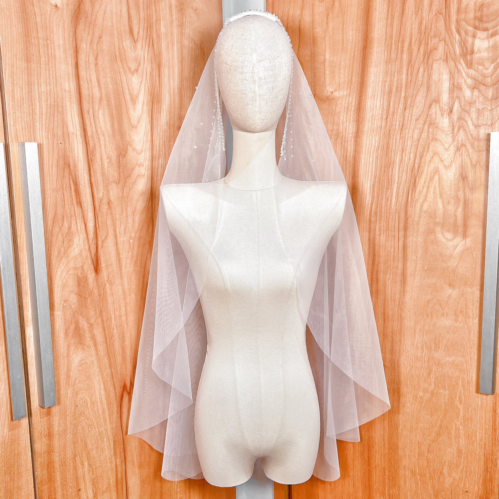 Front view of a fingertip-length Crystal Edge Mantilla Wedding Veil with shimmering scalloped lace draped over a mannequin.