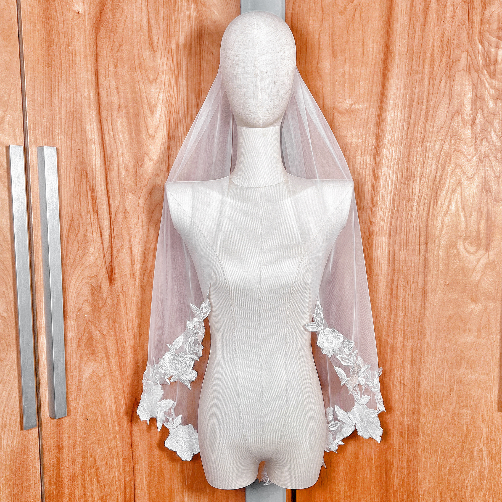 Front view of a fingertip-length wedding veil with floral appliqué on a mannequin, showcasing delicate ivory lace flowers on soft tulle.