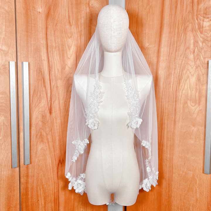 Fingertip length floral beaded lace wedding veil displayed on a mannequin for a romantic bridal look.