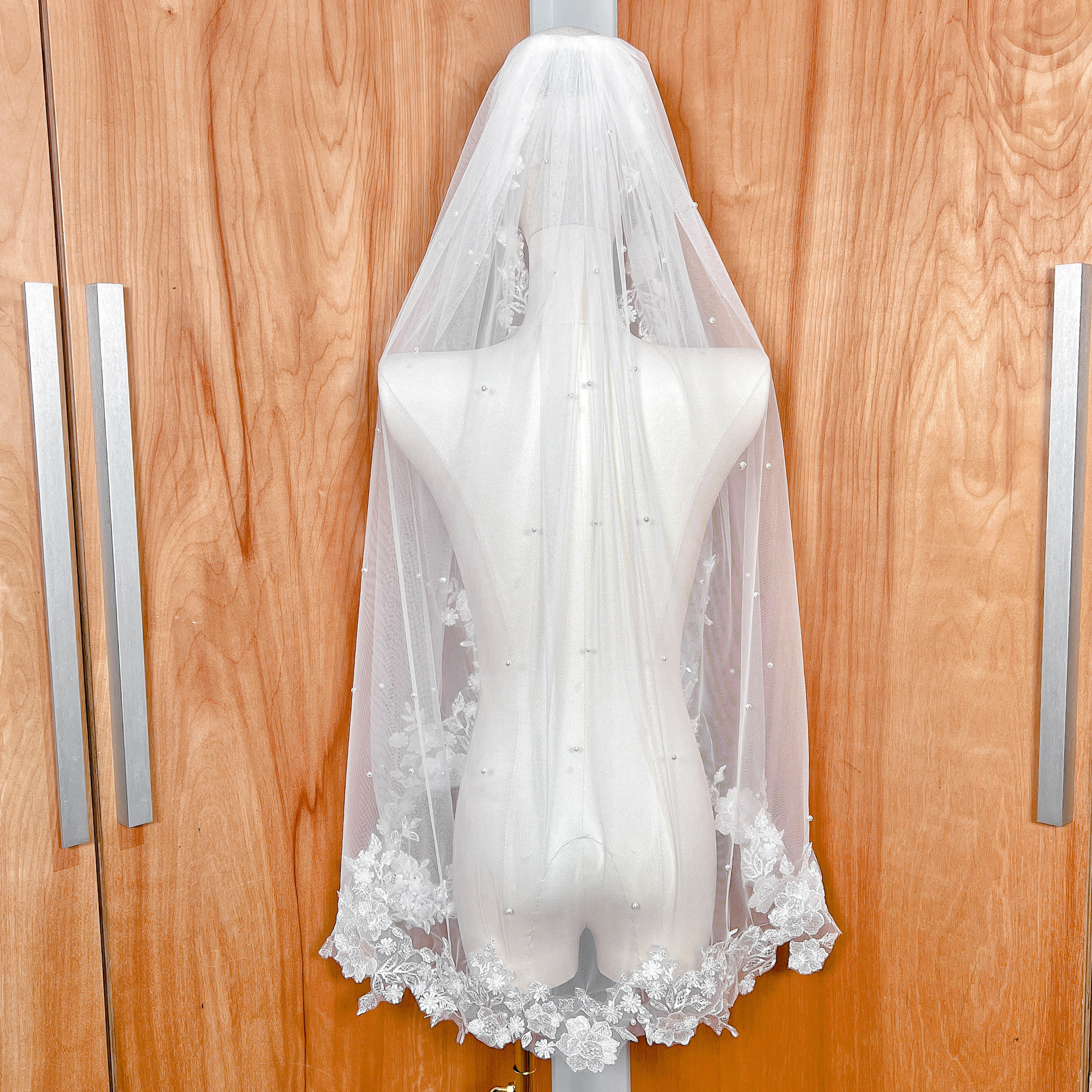 Back view of an ivory pearl and lace wedding veil displayed on a mannequin, showing the graceful drape and mid-length fingertip finish.