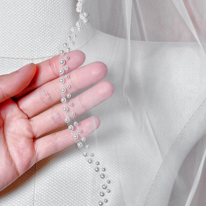 Close-up of a scalloped bridal veil featuring a finely beaded pearl trim and soft tulle in fingertip length.