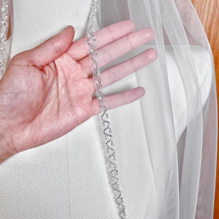 Close-up of the shimmering pearl beaded trim on a soft tulle fingertip bridal veil.