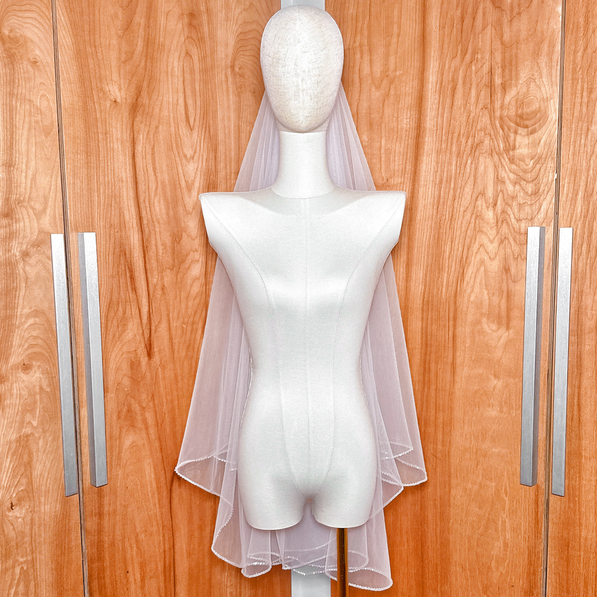 Elegant two tier wedding veil with rhinestone edge shown in fingertip length against a neutral background.
