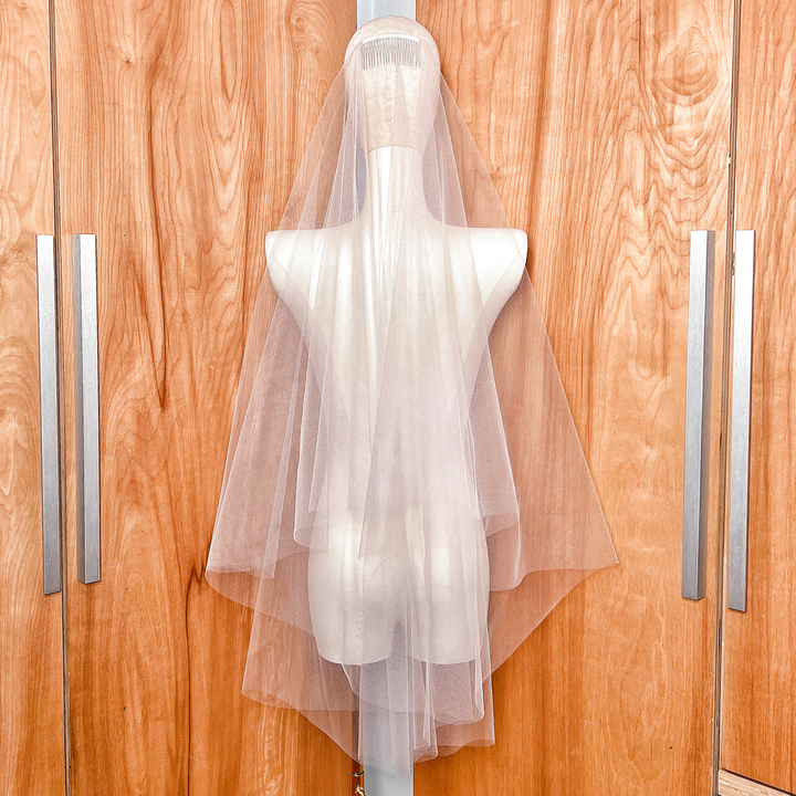 Close-up view of the sheer tulle fabric on a two-tier fingertip length veil with a raw edge.