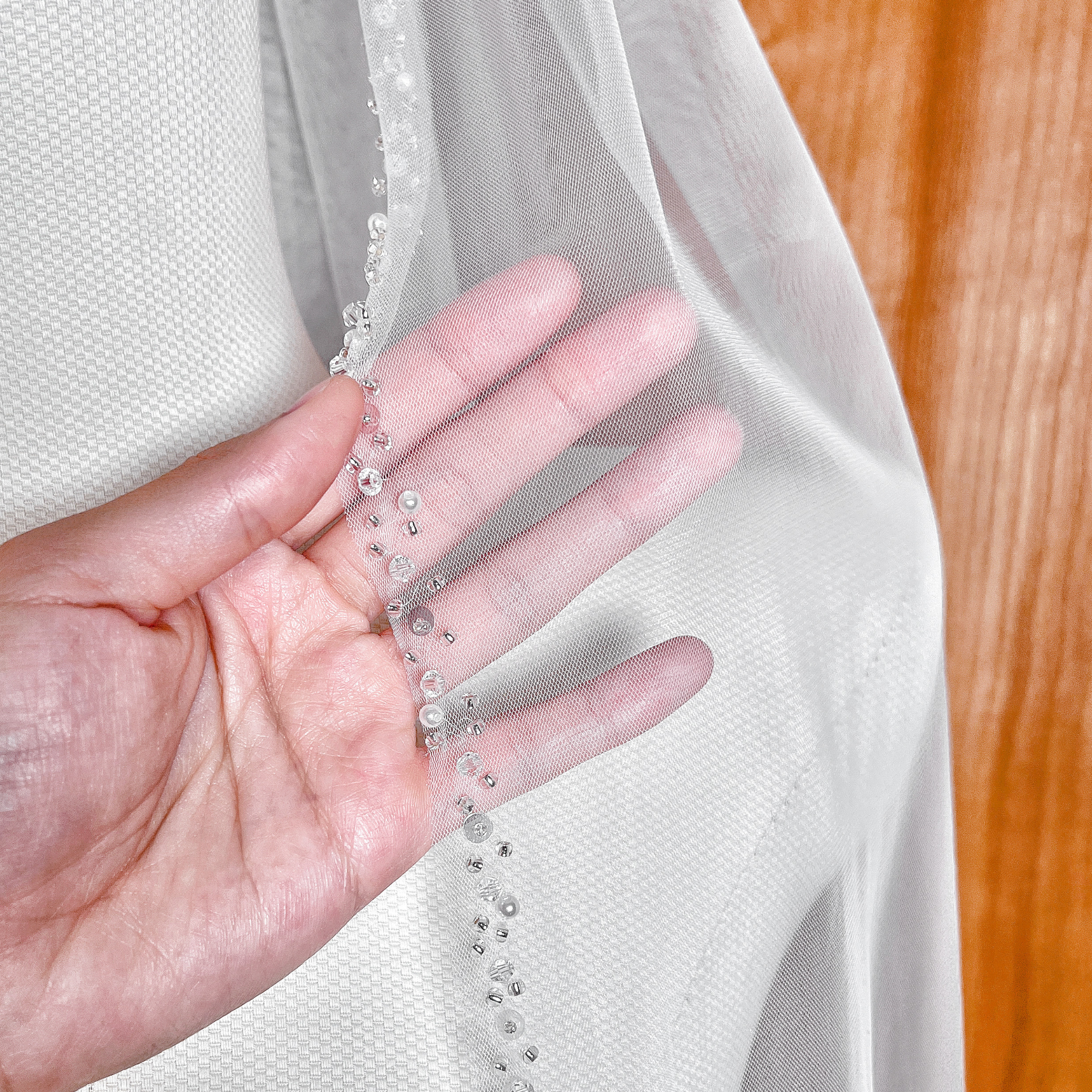 Close-up shot of the intricate pearl and crystal beaded edge on a fingertip length wedding veil.