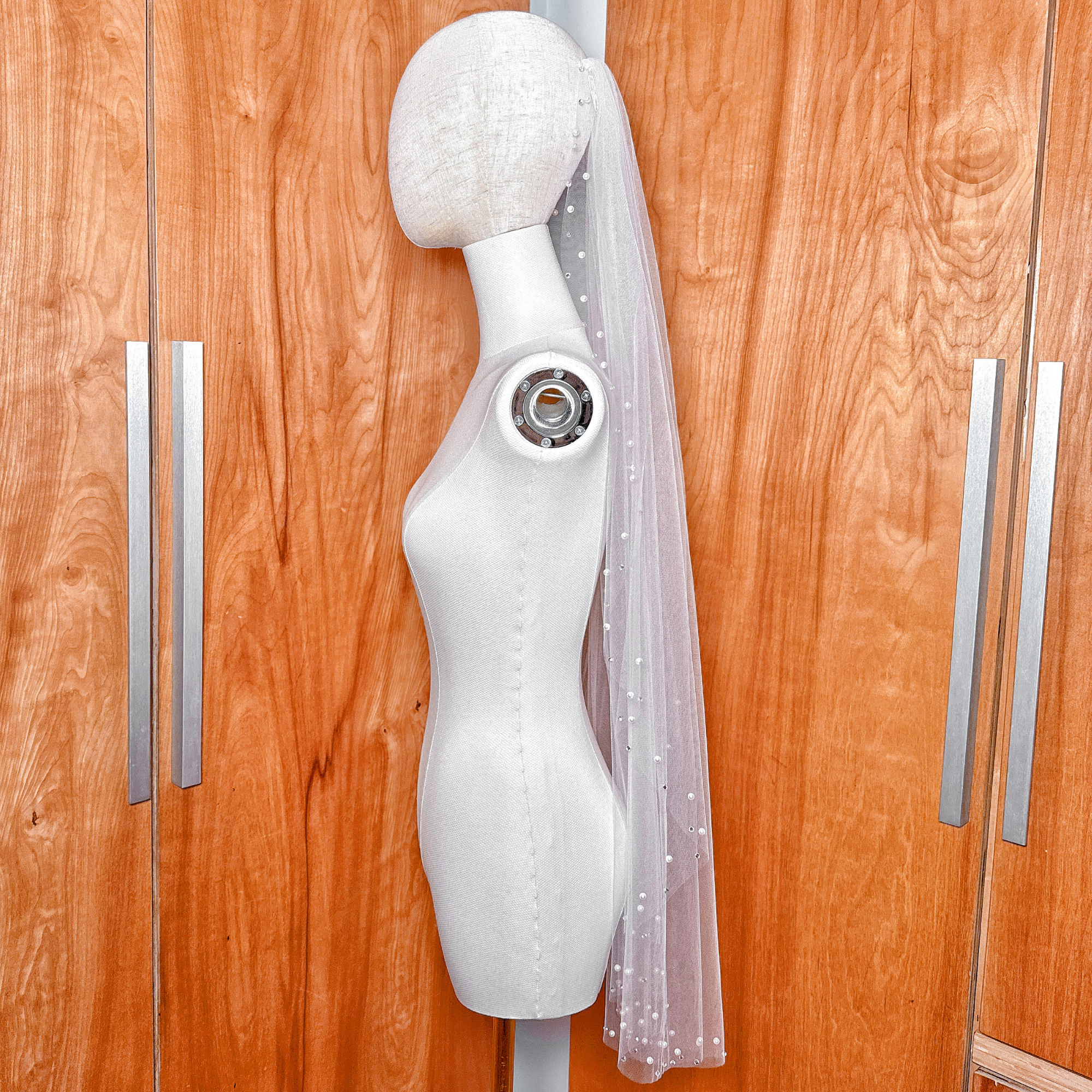 Detailed view of the intricate pearl and rhinestone embellishments on the edge of a fingertip length bridal veil.