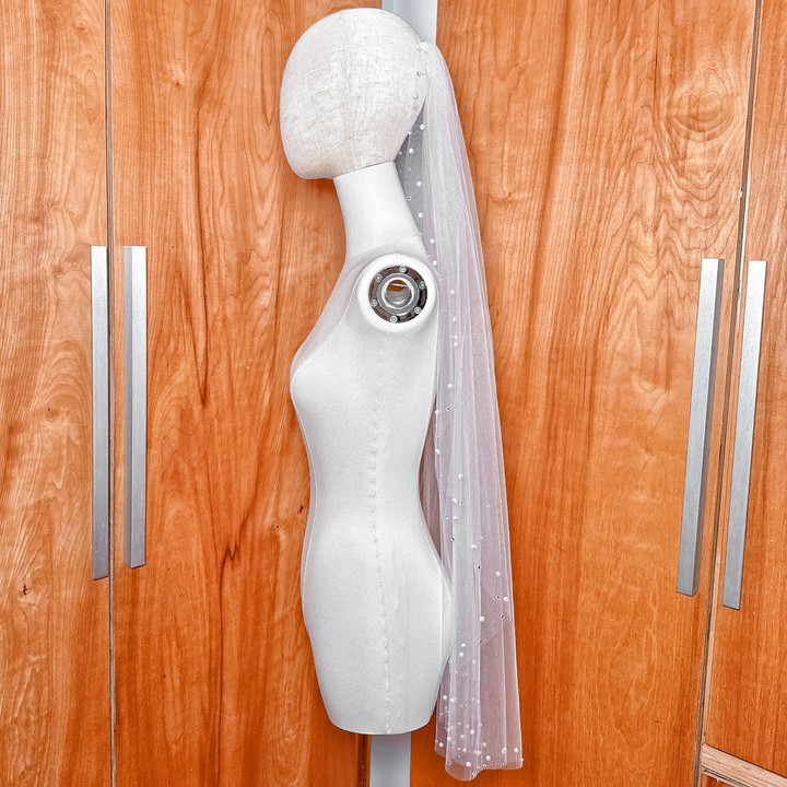 Detailed view of the intricate pearl and rhinestone embellishments on the edge of a fingertip length bridal veil.