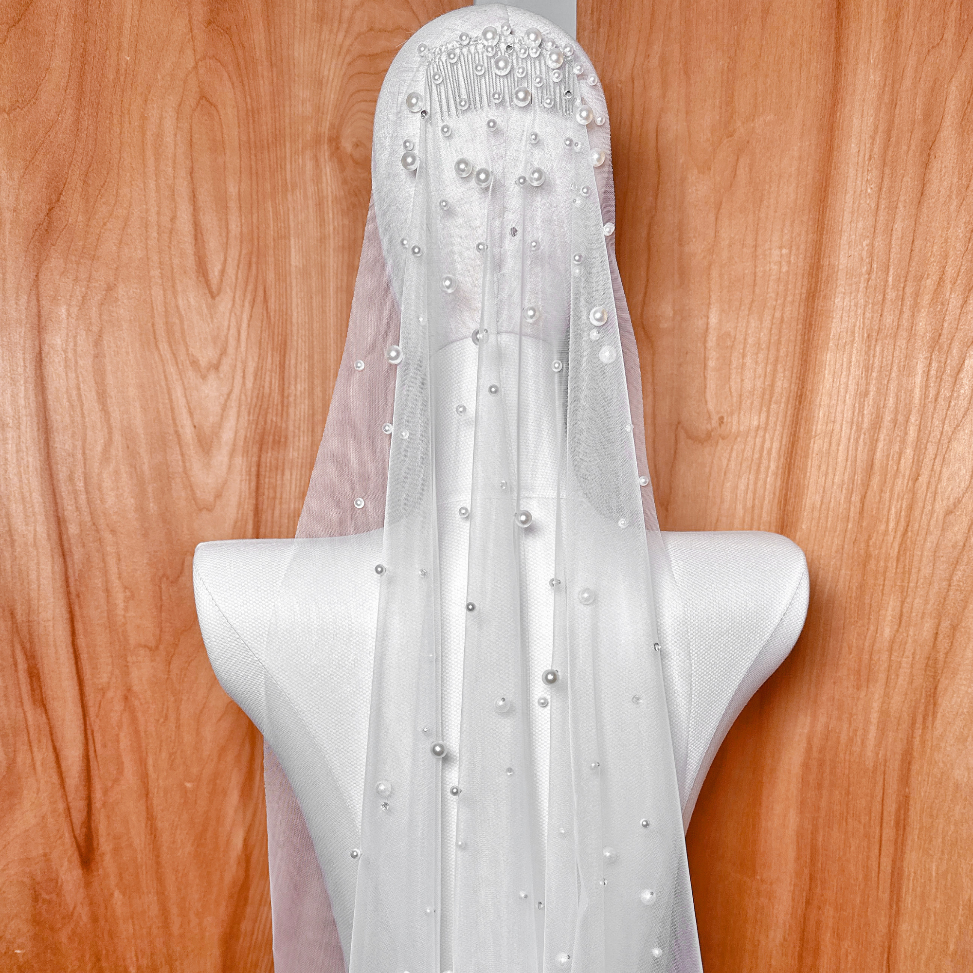 Close up detail of the intricate scattered rhinestone and pearl embellishments on a sheer fingertip length wedding veil.